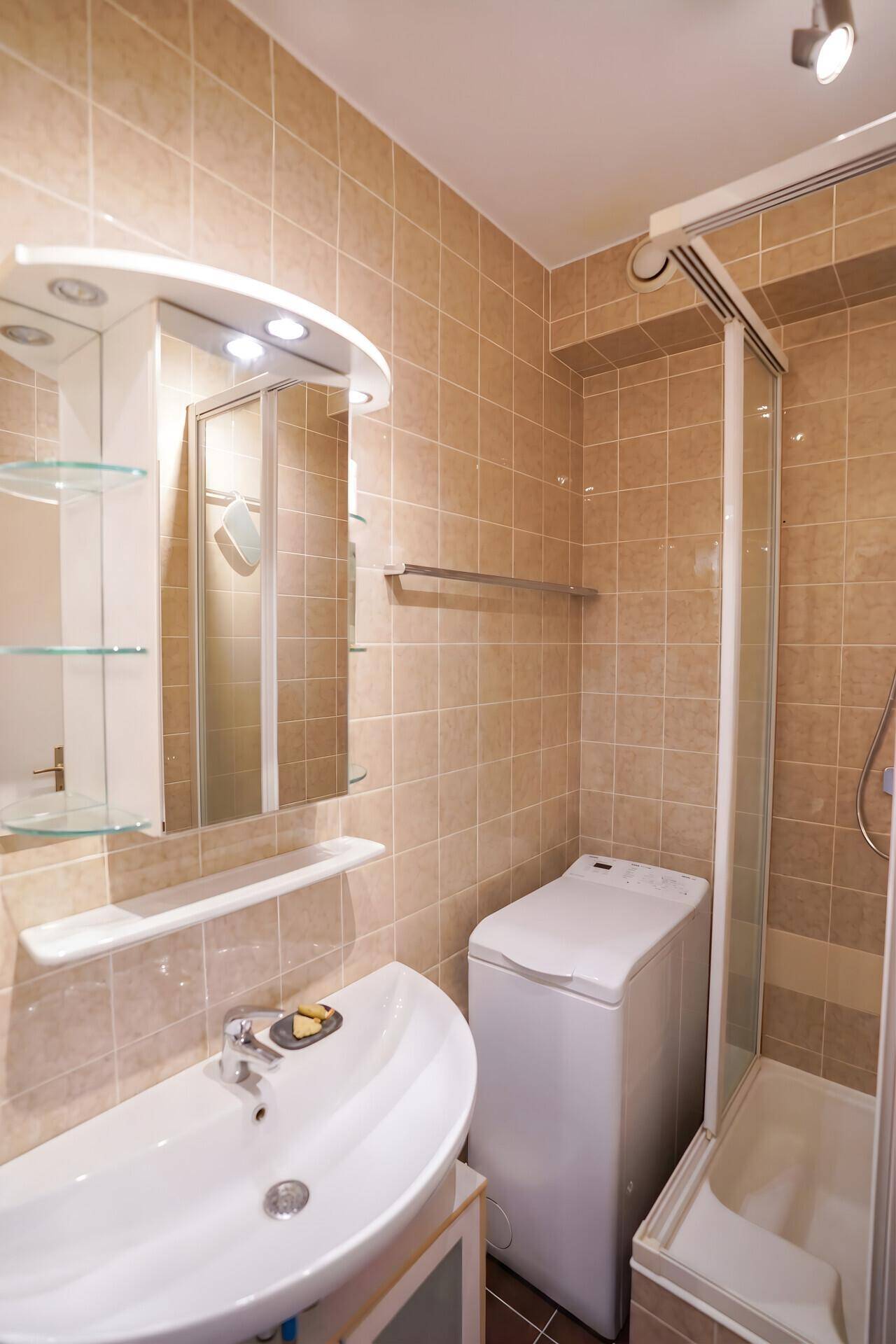 Gefliestes Badezimmer mit Dusche, Waschbecken und integrierter Waschmaschine.