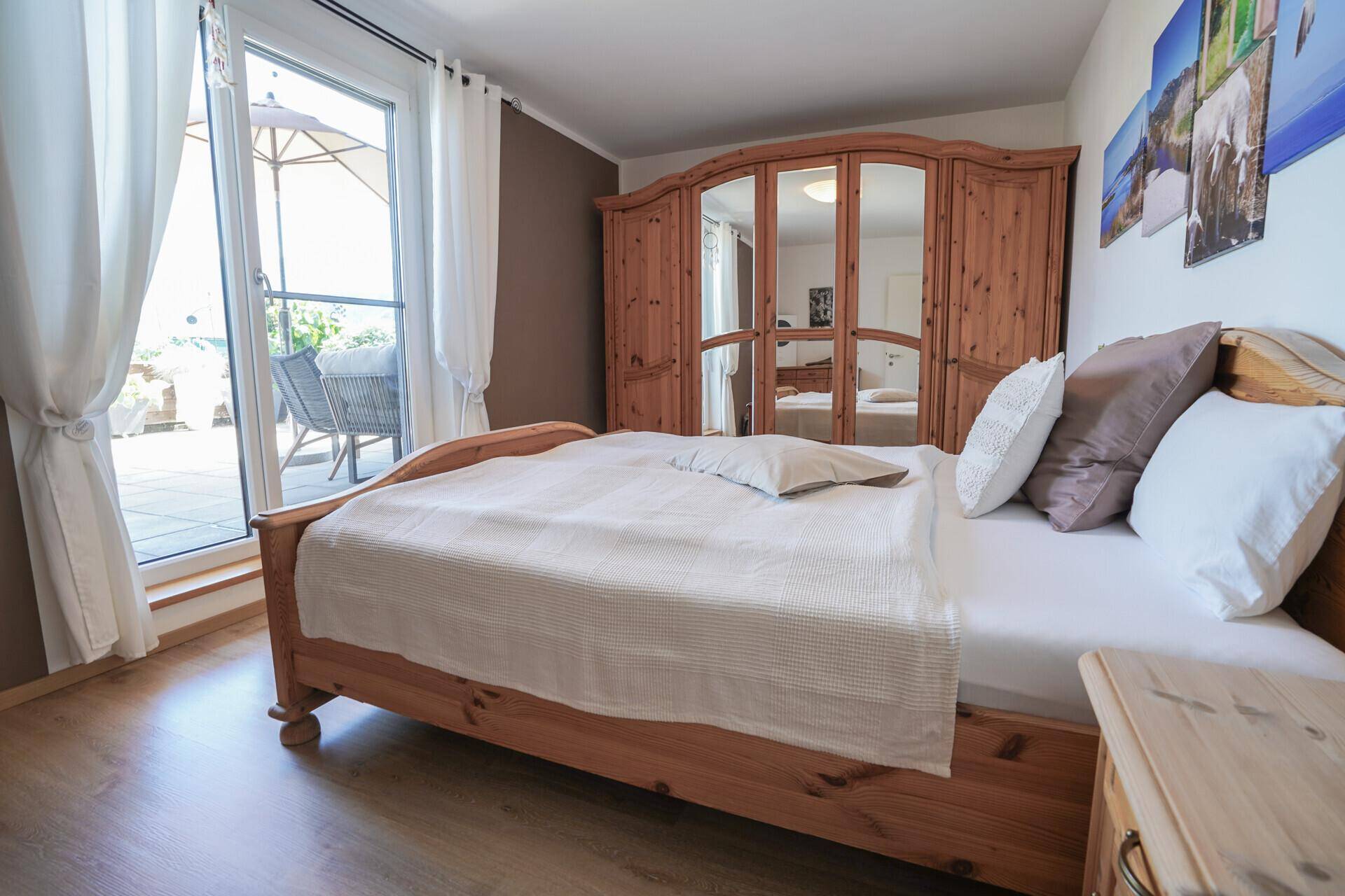 Gemütliches Schlafzimmer mit Holzbett, Spiegelschrank und Zugang zur Terrasse.