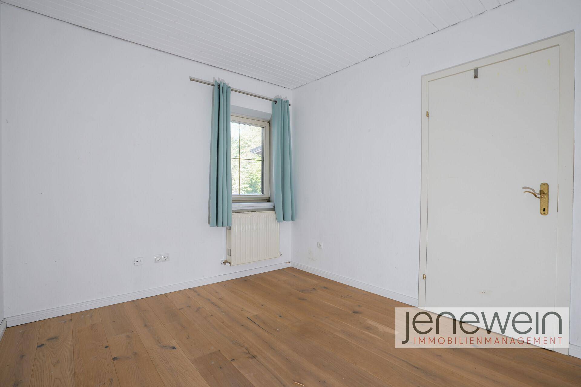 Schlichtes Schlafzimmer mit Holzboden und Fenster, ideal als Kinder- oder Gästezimmer.