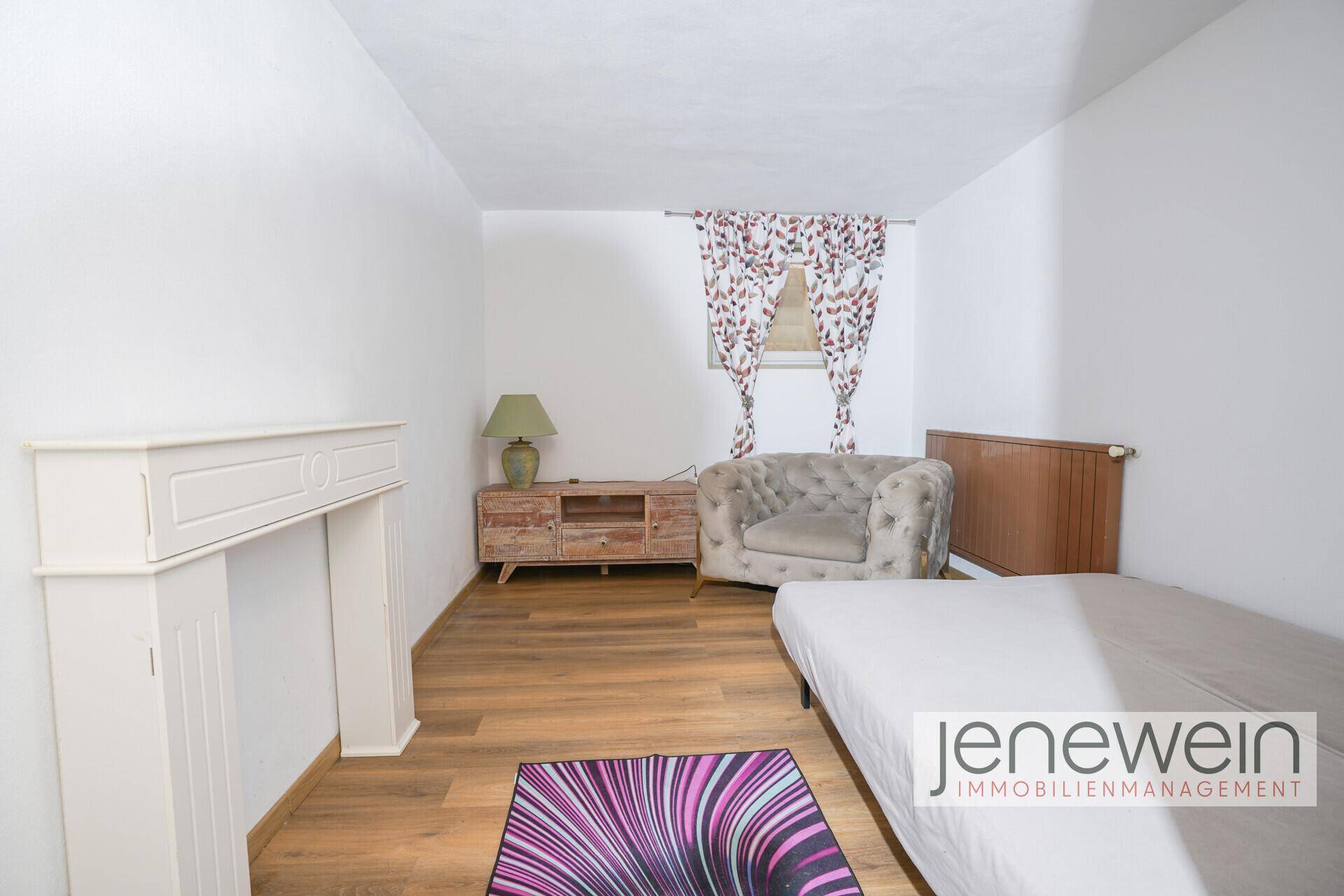 Helles Schlafzimmer mit Holzboden, dekorativem Kamin und bequemer Sitzgelegenheit.