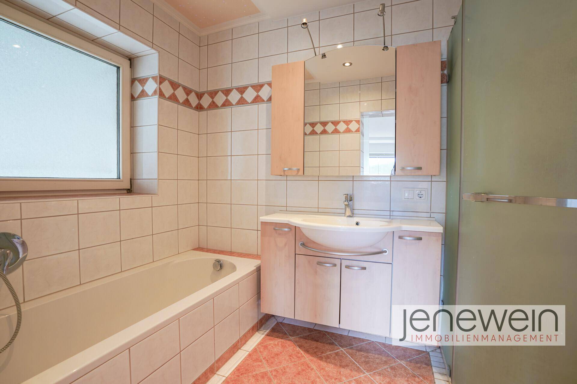 Badezimmer mit Badewanne, Waschtisch und hellen Fliesen.