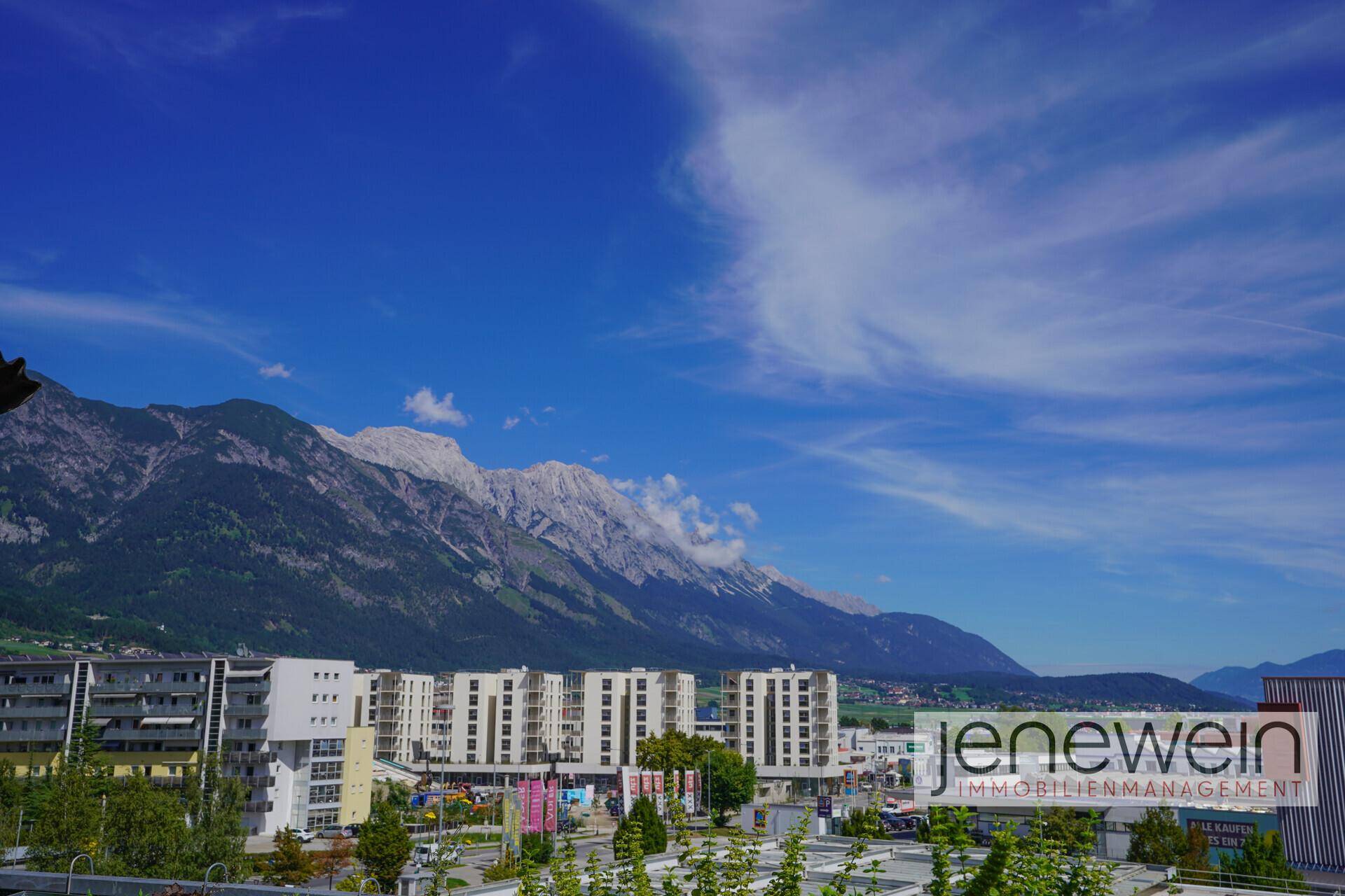 Panoramablick auf die Stadt und die umliegenden Berge unter blauem Himmel.