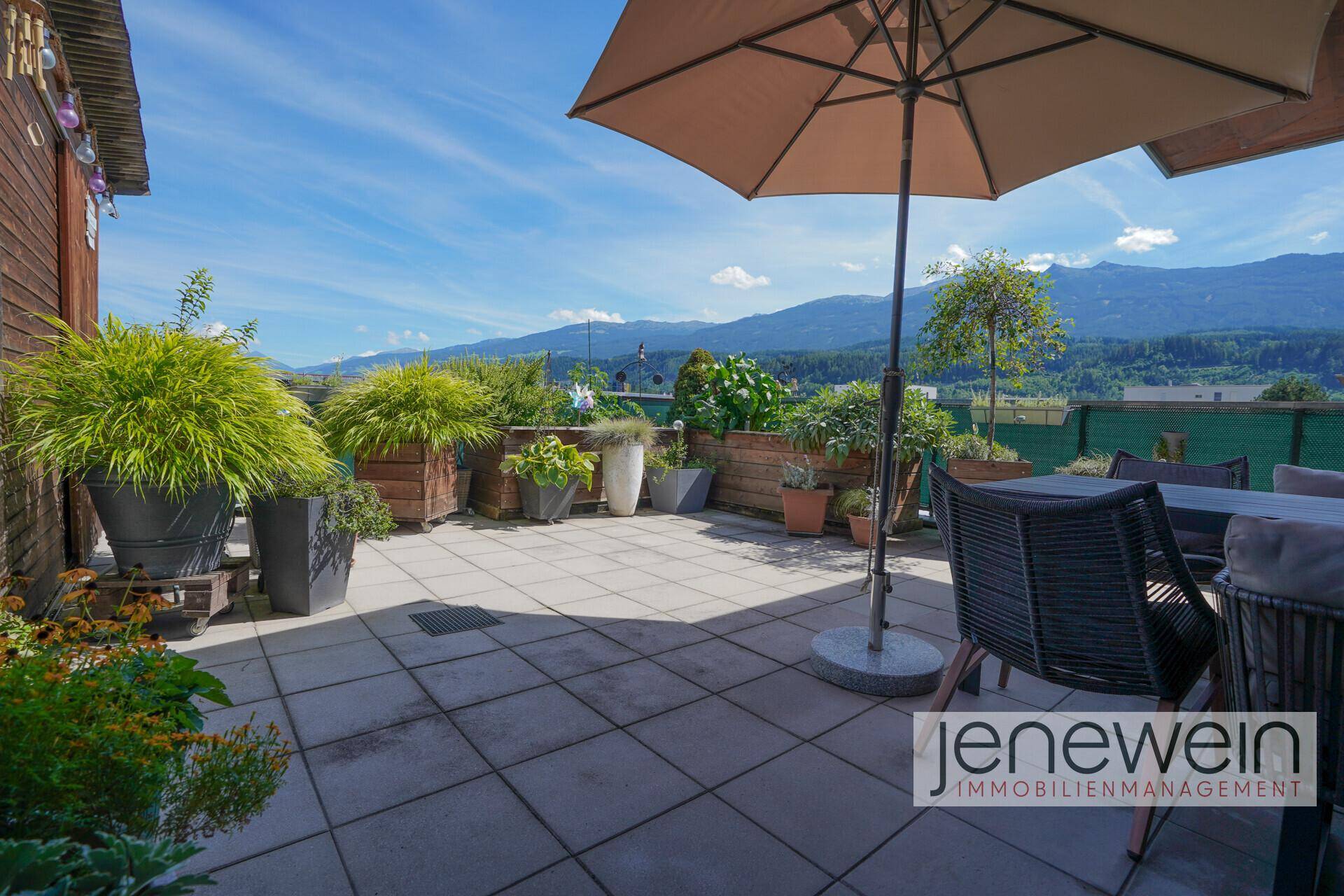 Geräumige Dachterrasse mit Sitzbereich, Sonnenschirm und weitem Bergblick.