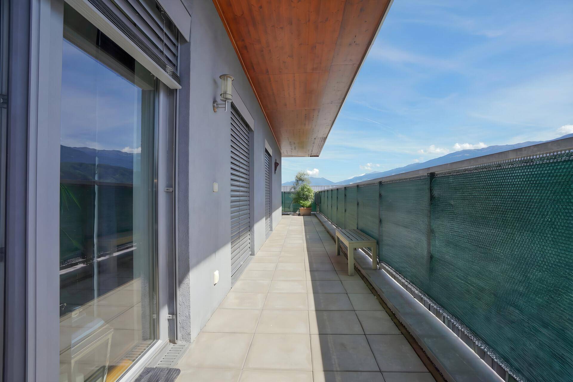 Langer Balkon mit Fliesenboden und Bergblick, geschützt durch eine grüne Abgrenzung.