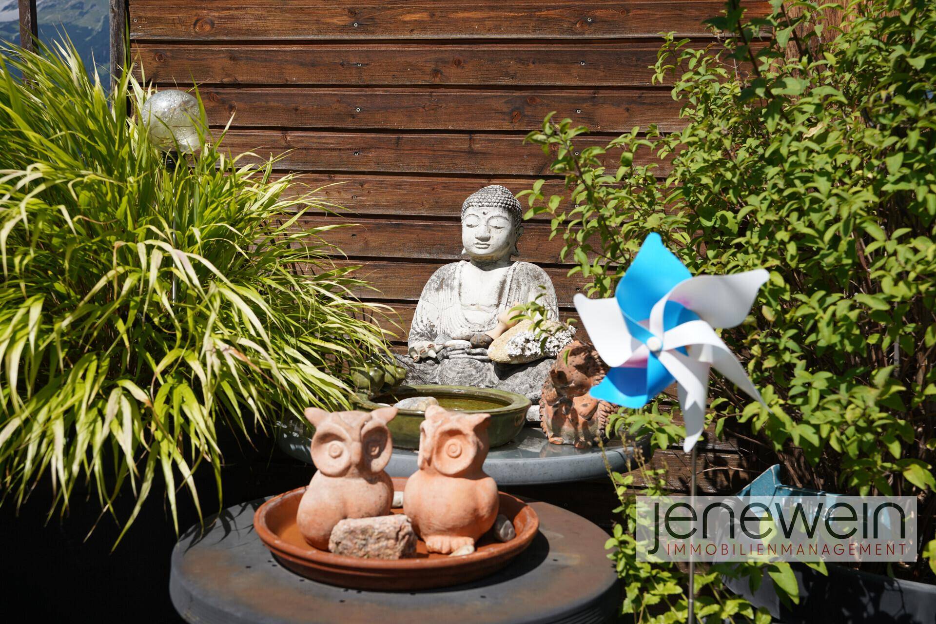 Dekorative Elemente auf der Terrasse, darunter eine Buddha-Statue und Pflanzen.