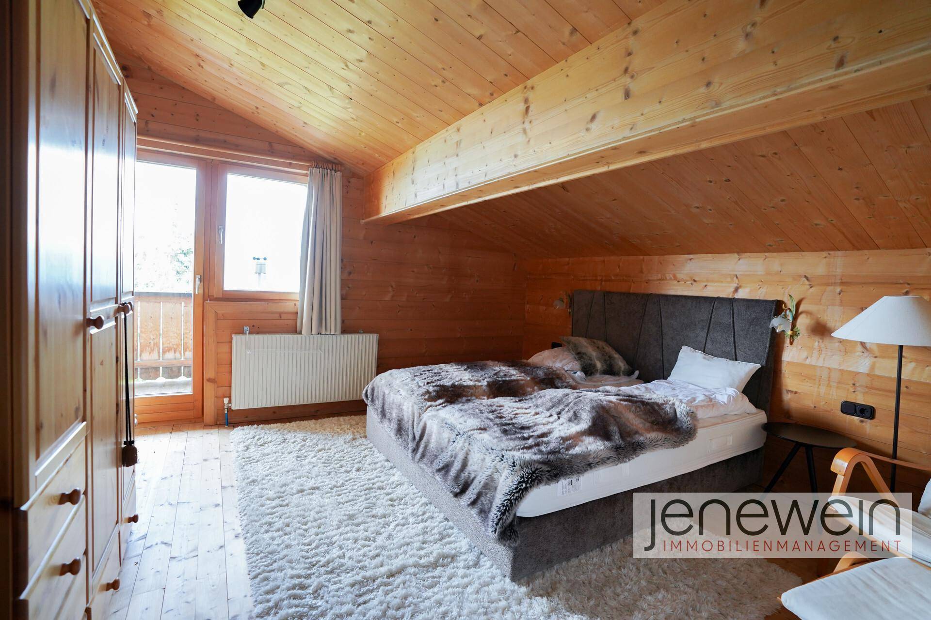 Schlafzimmer mit Holzboden, Dachschräge, Doppelbett und Zugang zum Balkon.