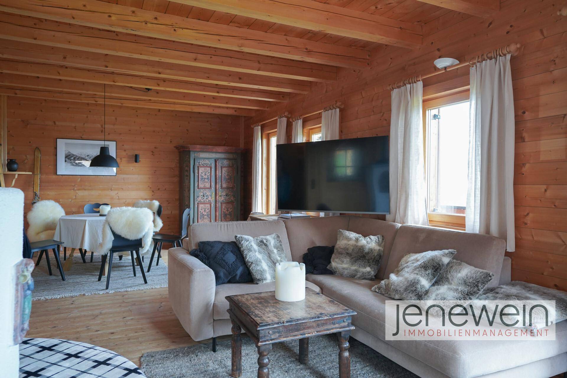 Geräumiges Wohnzimmer mit Holzbalkendecke, großem Sofa und Essbereich im Hintergrund.