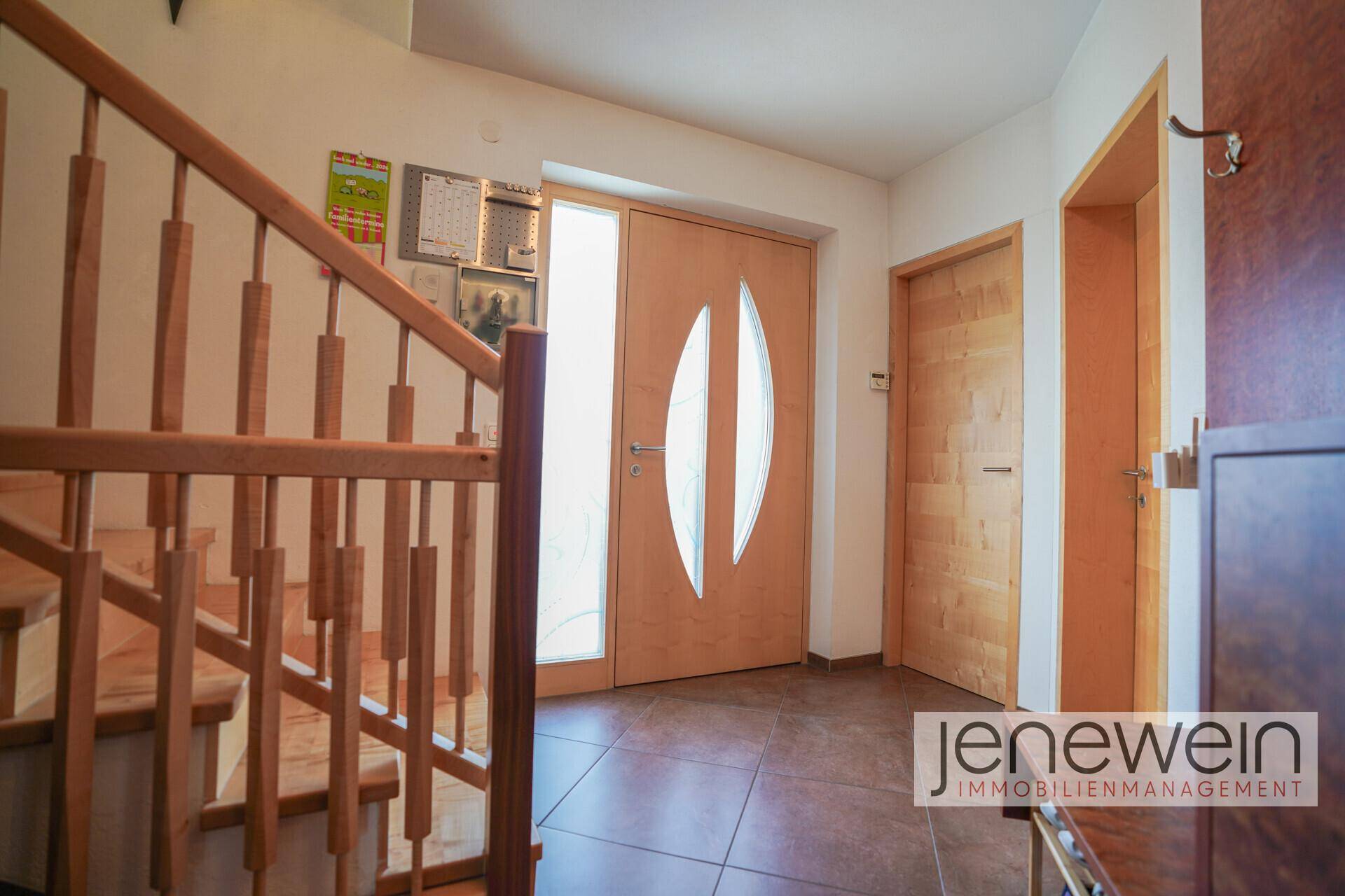 Heller Eingangsbereich mit Fliesenboden, Holztreppe und moderner Haustür mit Glaselementen.