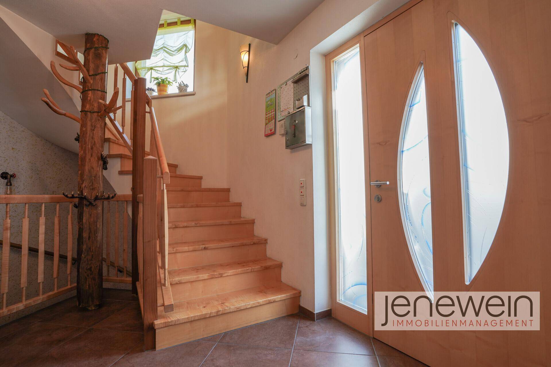 Geräumiger Flur mit Holztreppe, natürlichem Licht und rustikalem Baumstamm-Geländer als Blickfang.