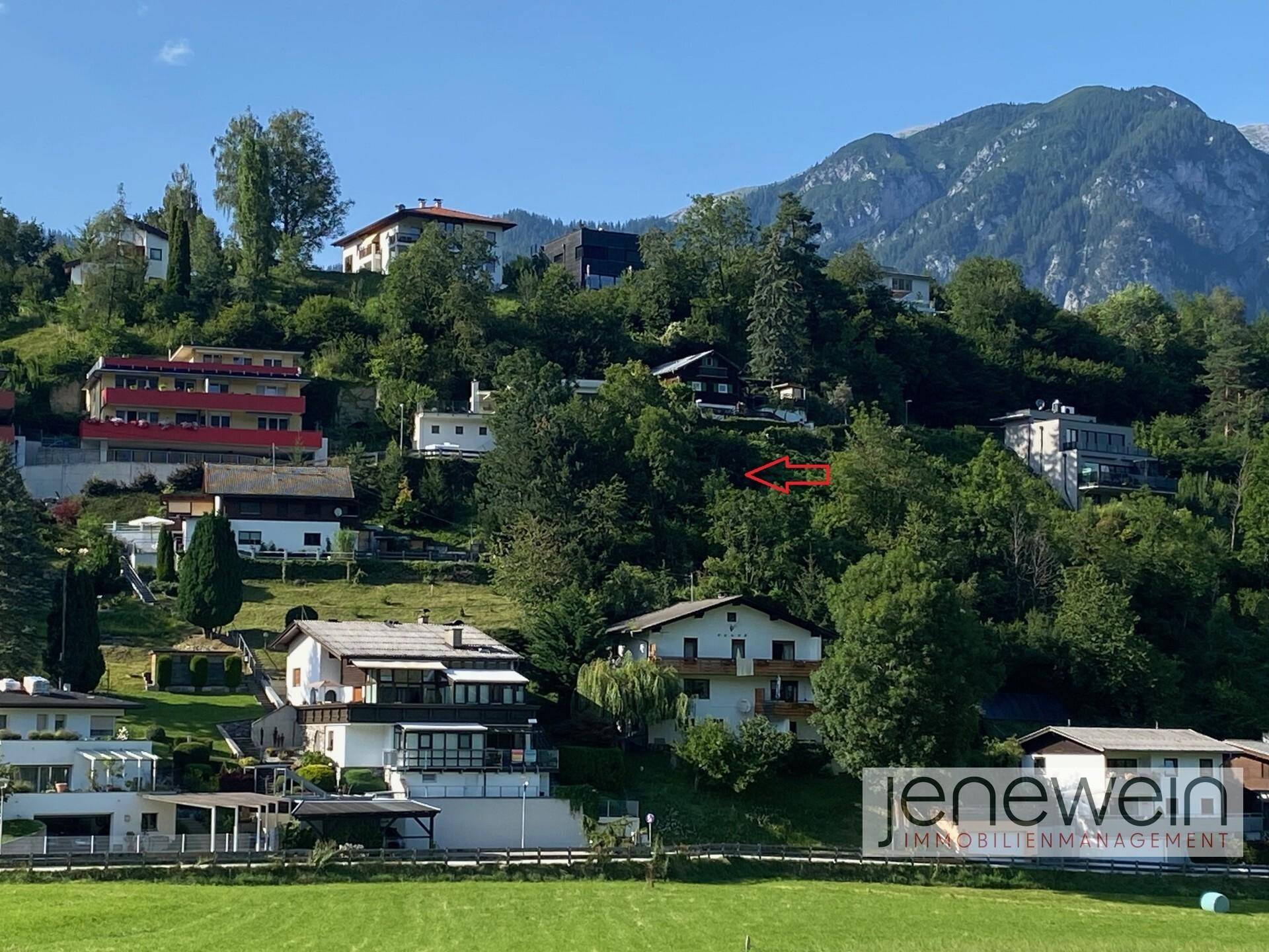 Aussicht auf eine idyllische Hanglage mit Wohnhäusern, umgeben von Bäumen und einer beeindruckenden Bergkulisse.