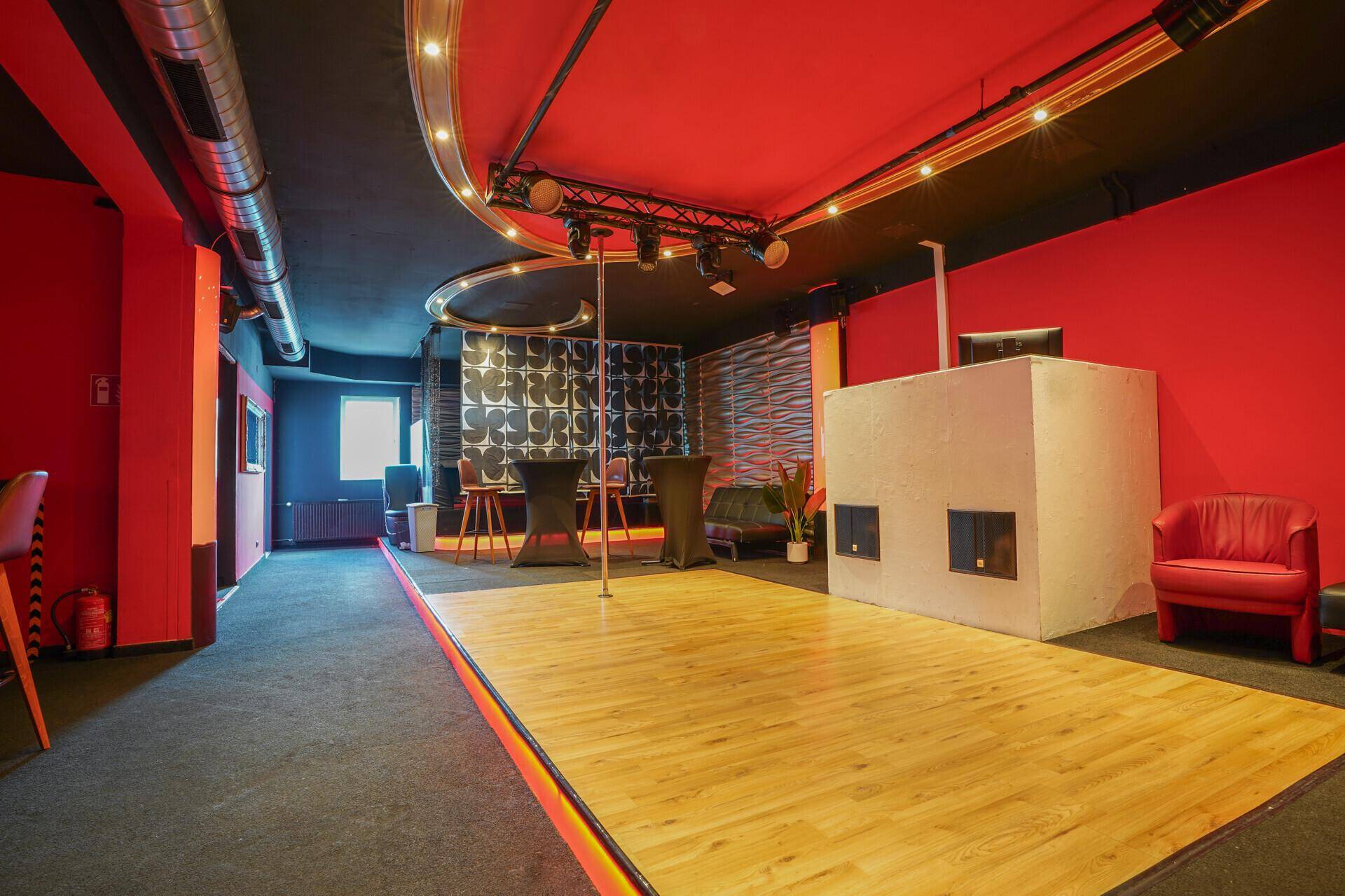 Großer Unterhaltungsraum mit Tanzfläche, Stange, roter Decke und schwarzem Teppichboden.