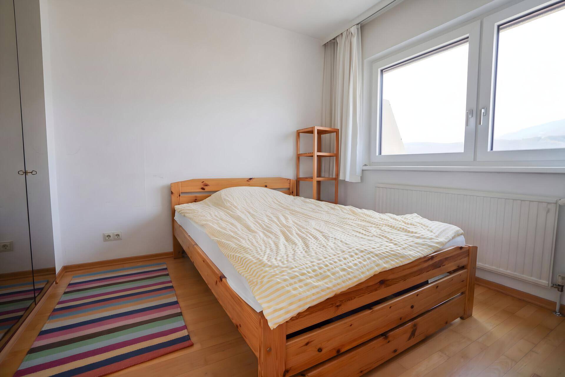 Möbliertes Schlafzimmer mit Holzbett, hellem Holzfußboden und farbigem Teppich.