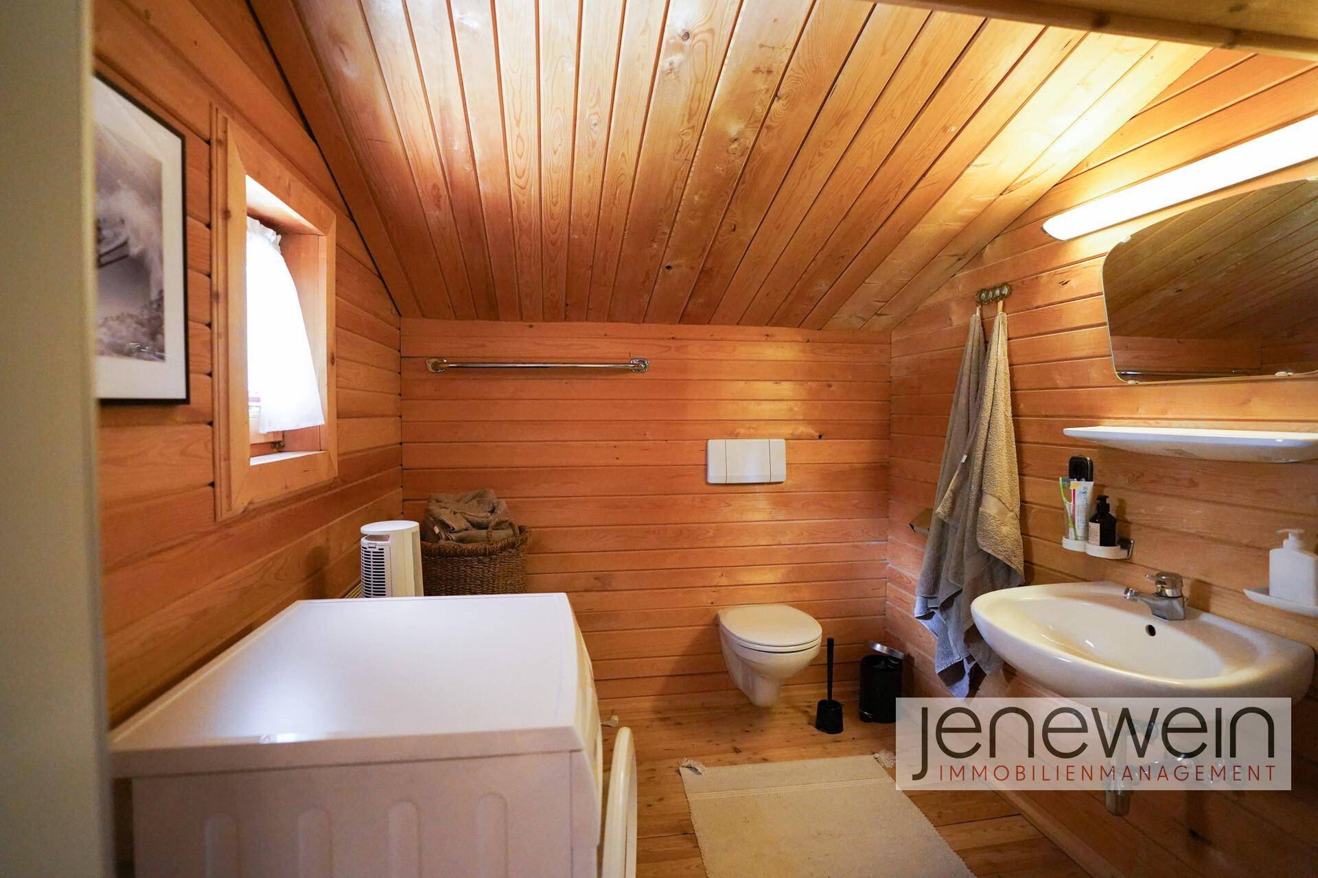 Badezimmer mit Holztäfelung, Dachschräge, WC, Waschbecken und Fenster.