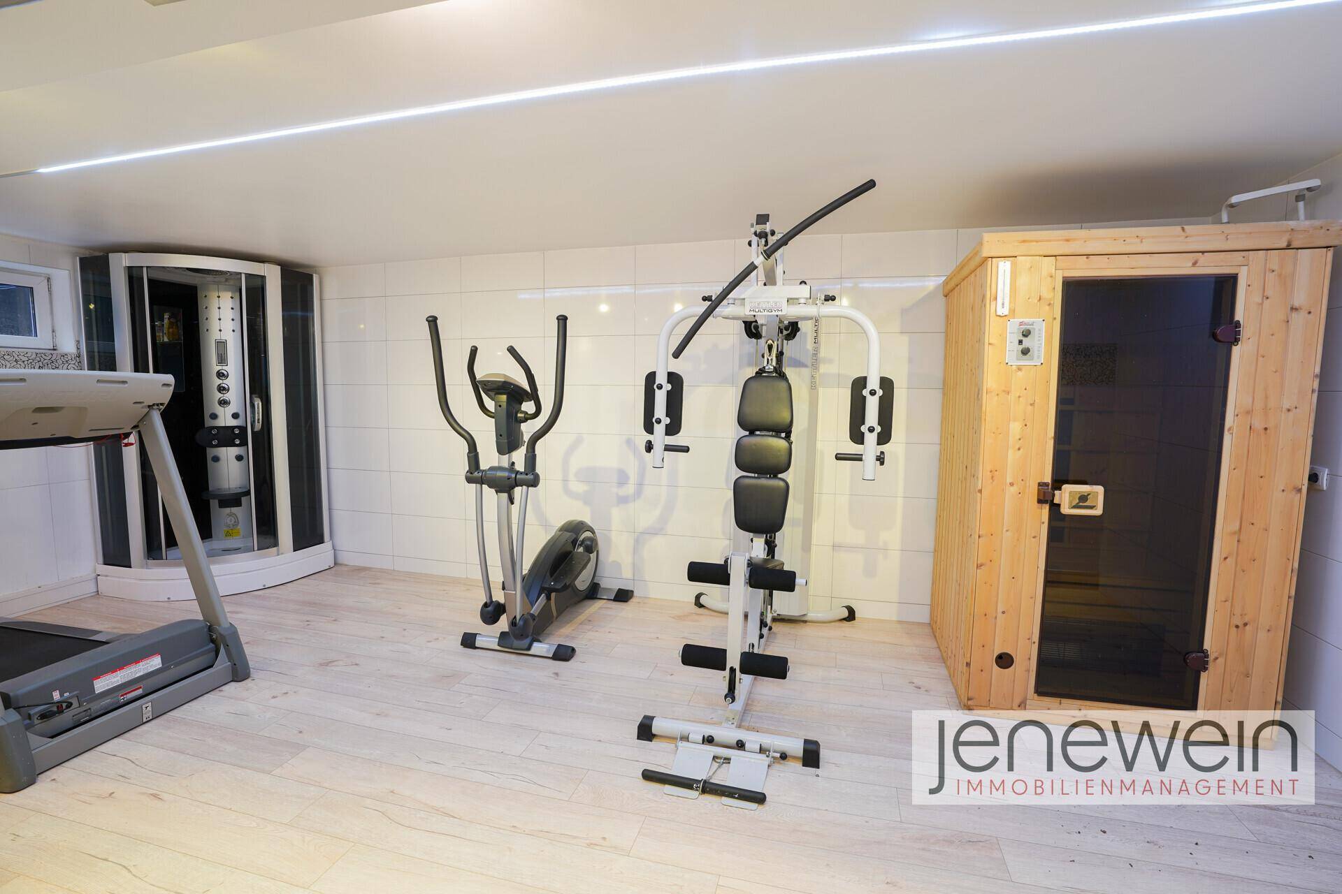 Fitnessraum mit verschiedenen Trainingsgeräten, einer Sauna und einer Duschkabine.