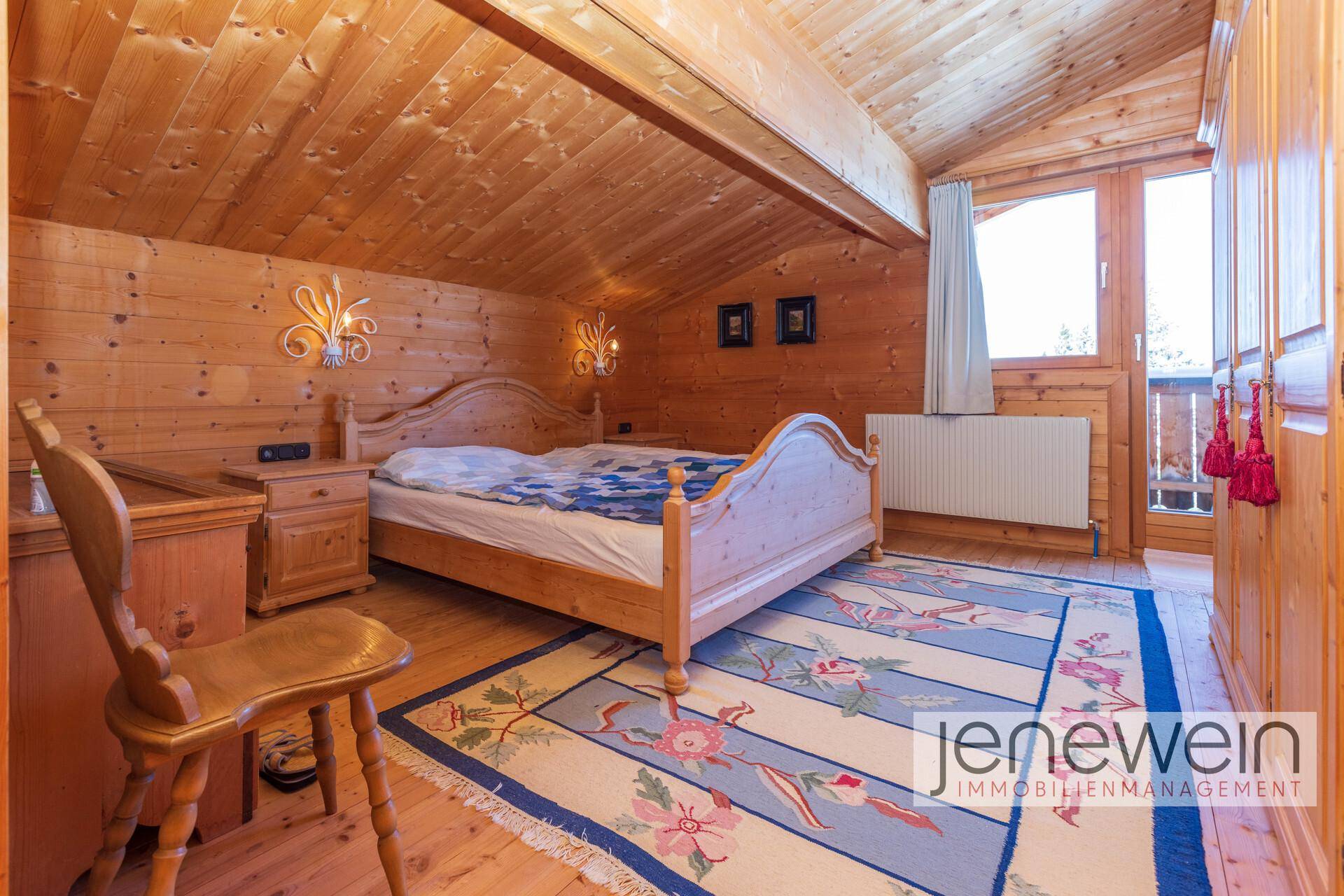 Traditionelles Schlafzimmer mit Holzbett, Dachschräge und farbenfrohem Teppich.