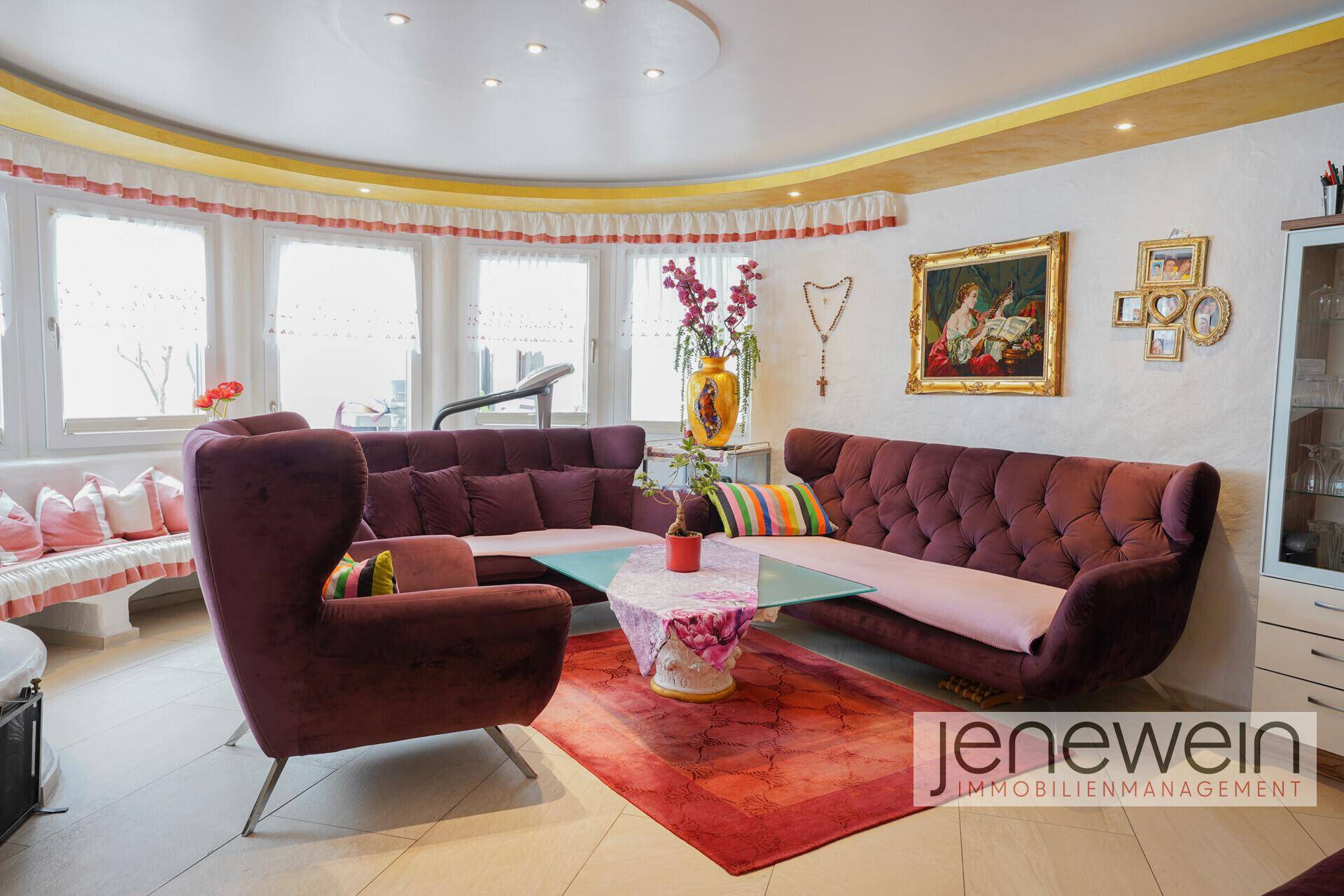 Farbenfrohes Wohnzimmer mit lila Sofas, großen Fenstern und heller Dekoration.