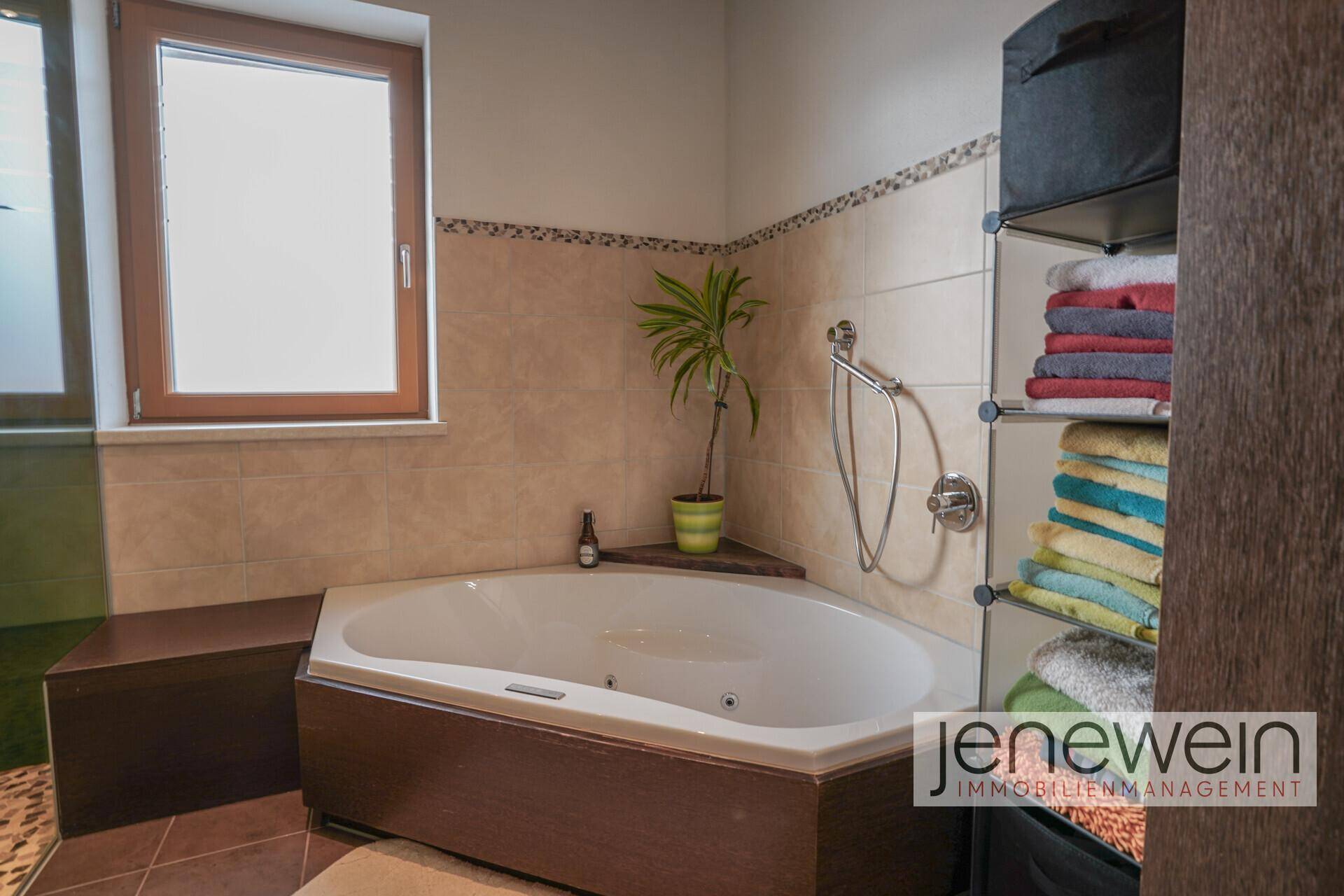 Eckbadewanne im Badezimmer mit Fliesenboden und praktischem Regal für Handtücher und Pflegeprodukte.