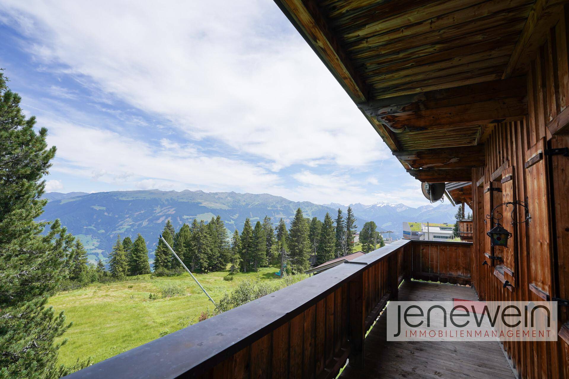 Geräumiger Holzbalkon mit weitem Blick auf die umliegende Berglandschaft und grüne Wiesen.