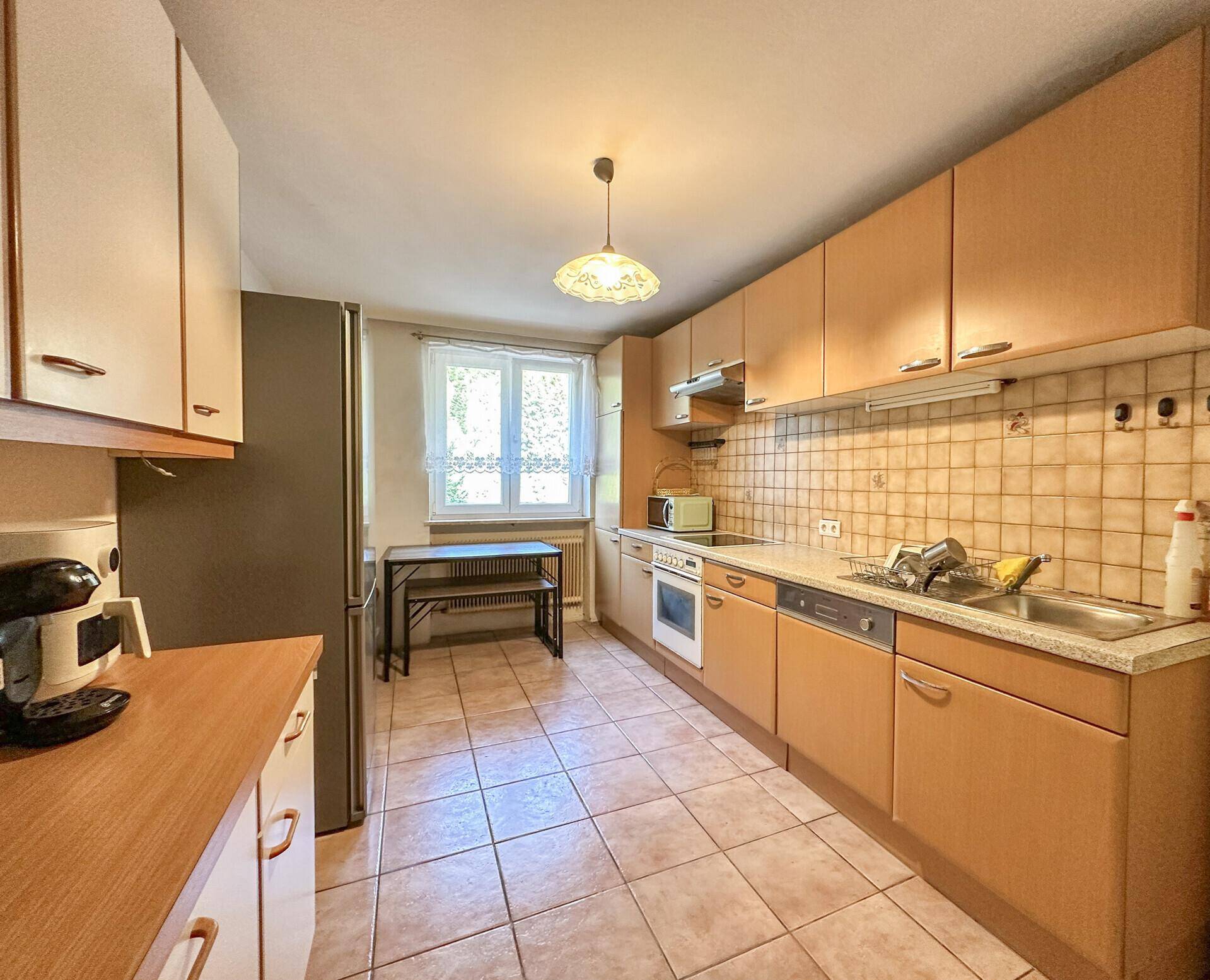Funktionale Küche mit Holzfronten, Fliesenboden, Fenster und integrierten Geräten.