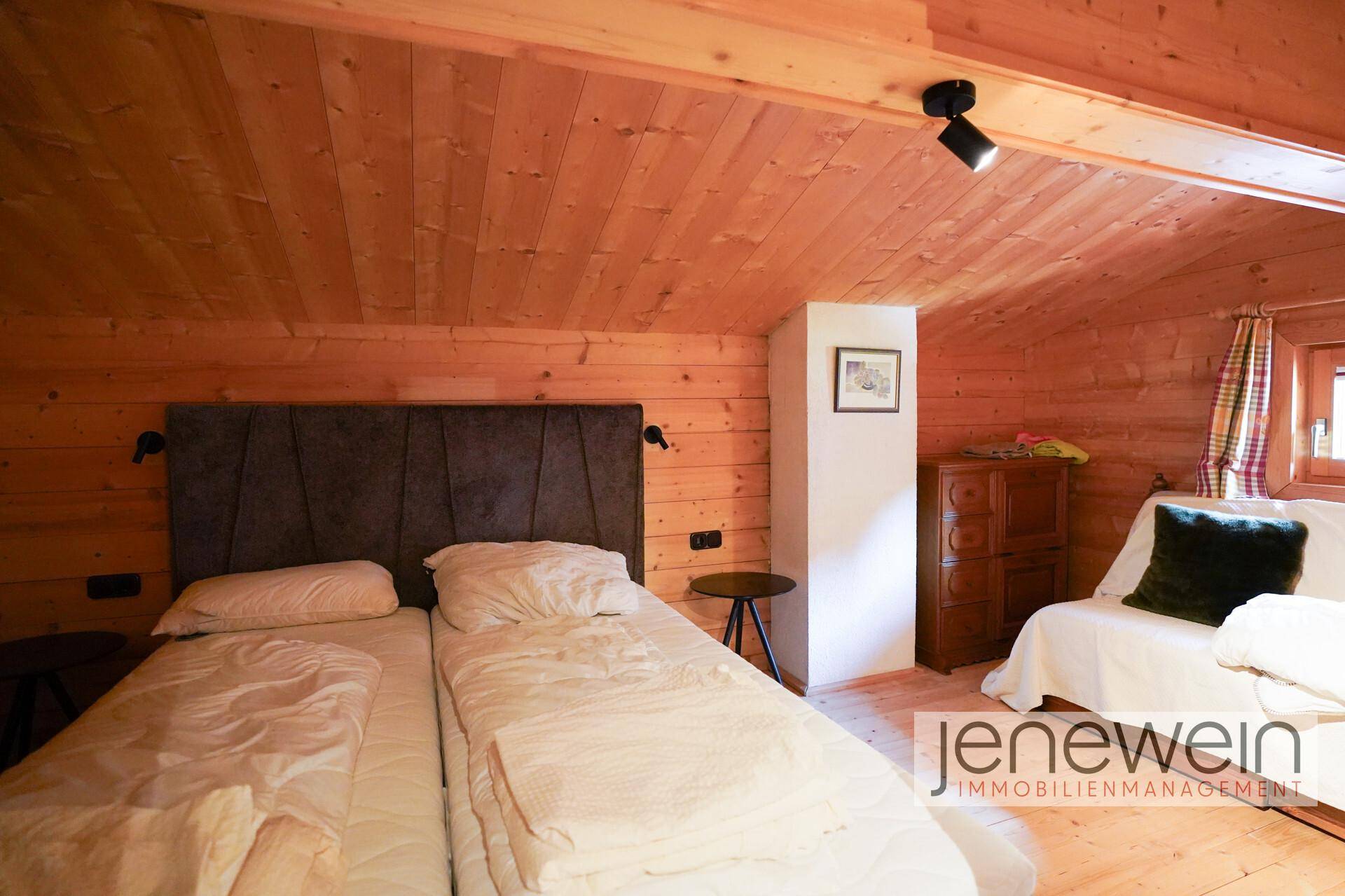 Gemütliches Schlafzimmer mit Holzwänden, Dachschräge und zwei Einzelbetten.