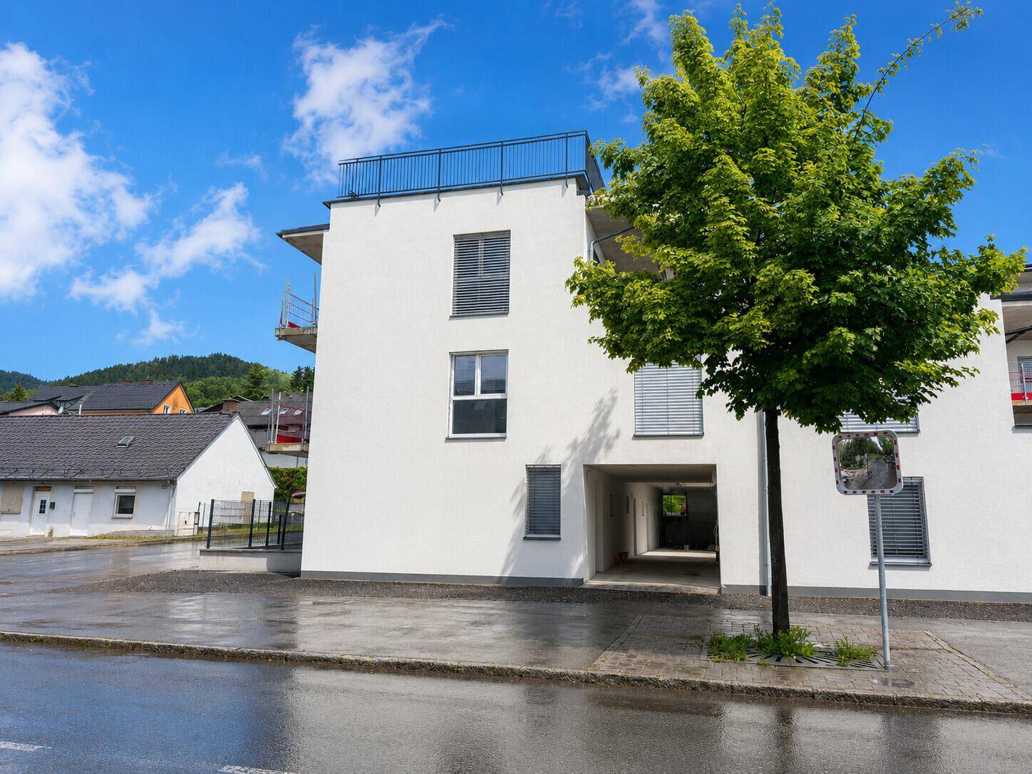 Ansicht des modernen Wohngebäudes mit weißer Fassade, Baum und Einfahrt unter blauem Himmel.