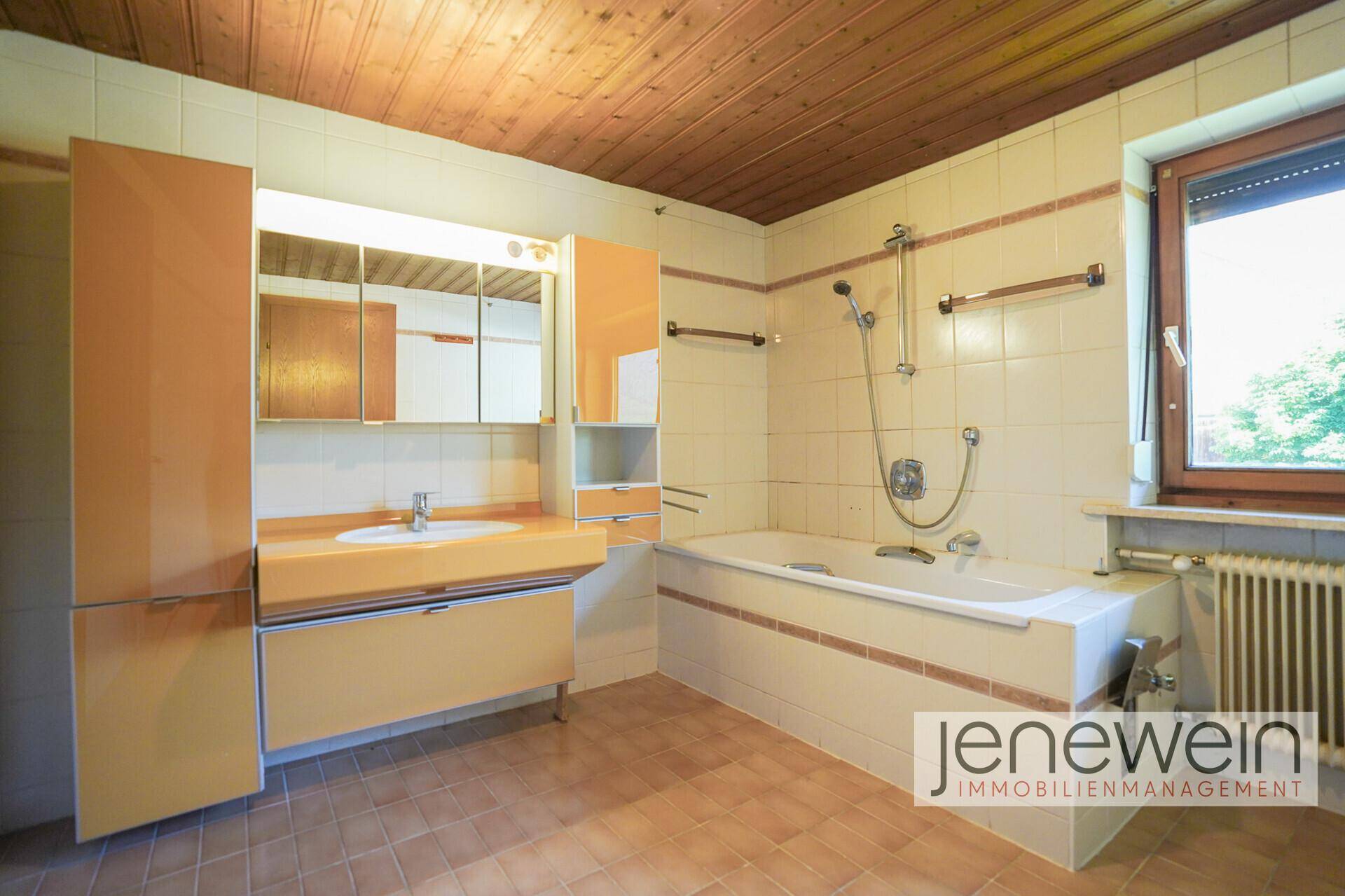 Helles Badezimmer mit Badewanne, Waschtisch und Spiegelschrank, ausgestattet mit Fenster.