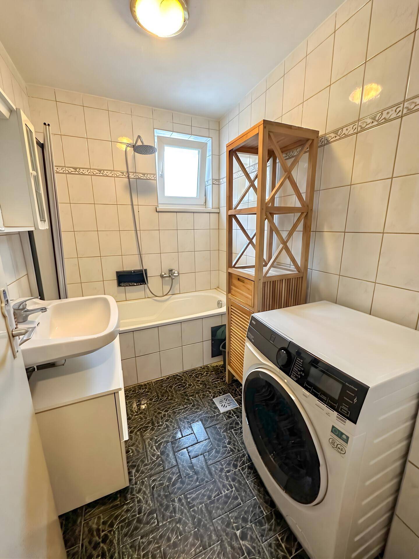 Badezimmer mit Badewanne, Waschbecken, Fliesen und einer Waschmaschine.