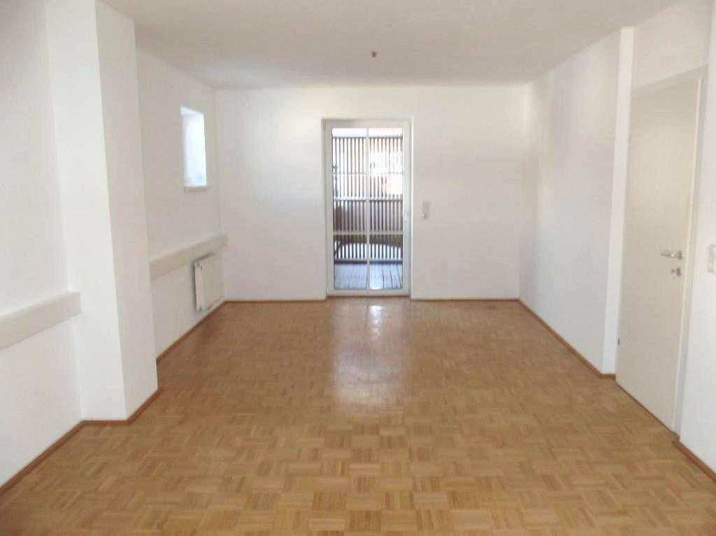 Geräumiger, leerer Raum mit Parkettboden und einer Tür, die zu einem weiteren Bereich führt.