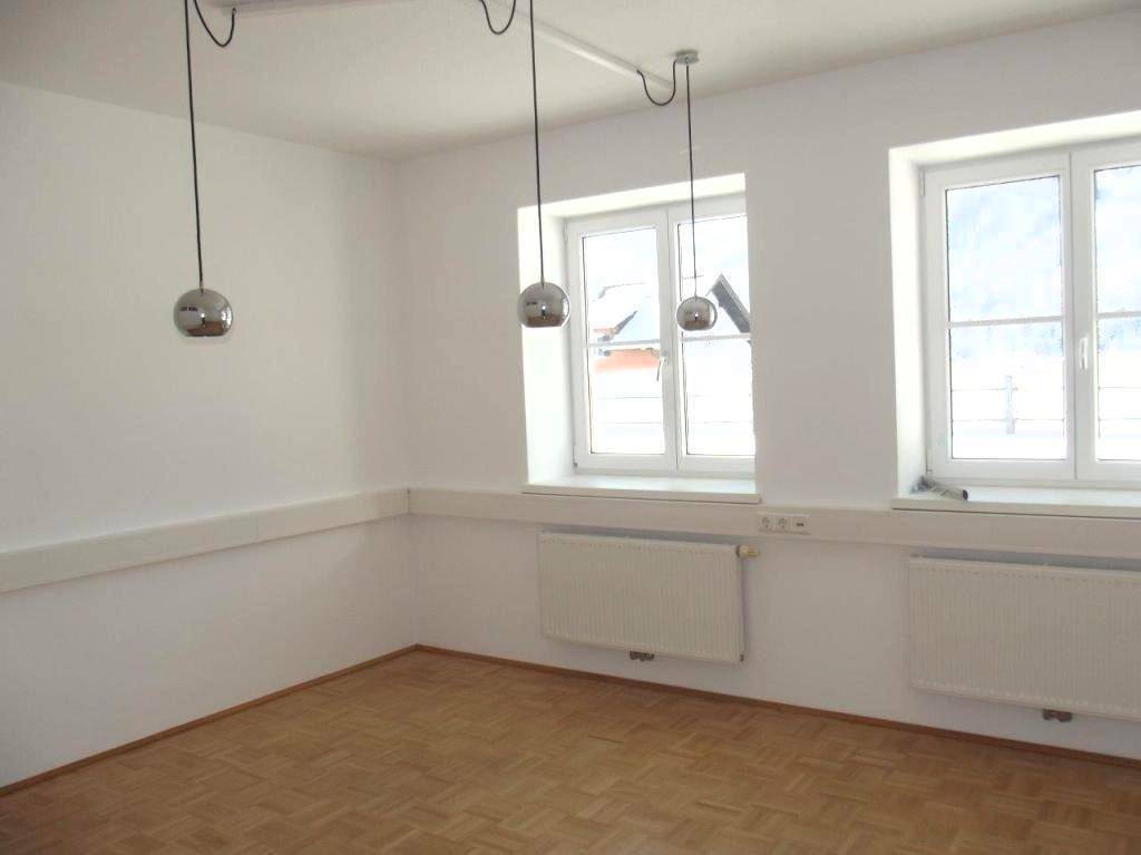 Leerer Raum mit Parkettboden, zwei großen Fenstern und modernen Hängelampen.
