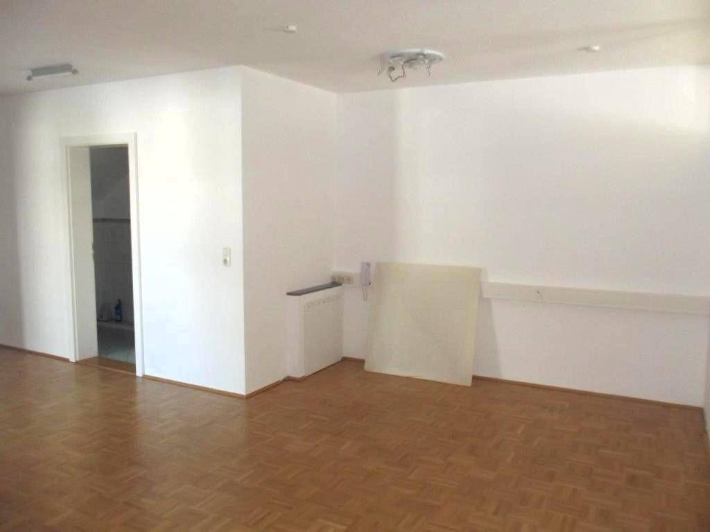Heller, leerer Raum mit Parkettboden und einem offenen Durchgang zu einem Nebenraum.