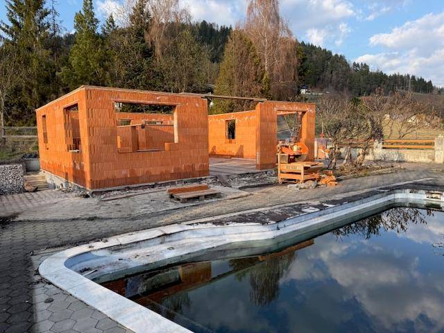 Rohbau eines Einfamilienhauses mit unverputzten Ziegelwänden und einem leeren Swimmingpool im Vordergrund.