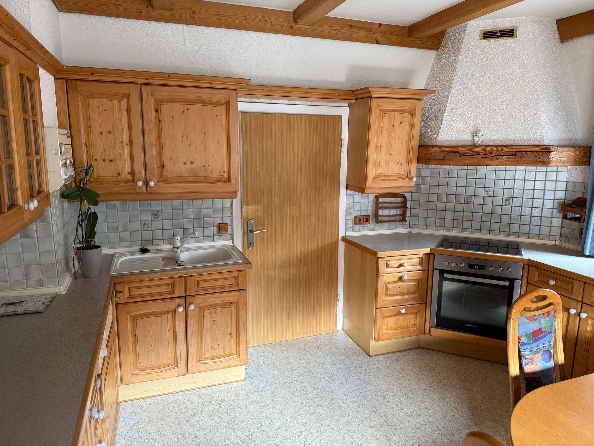 Traditionelle Küche mit Holzschränken, Fliesenrückwand und Holzbalkendecke.
