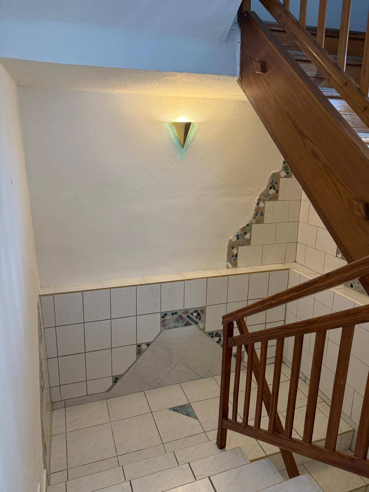 Geflieste Treppe mit Holzgeländer und dekorativen Wandfliesen.
