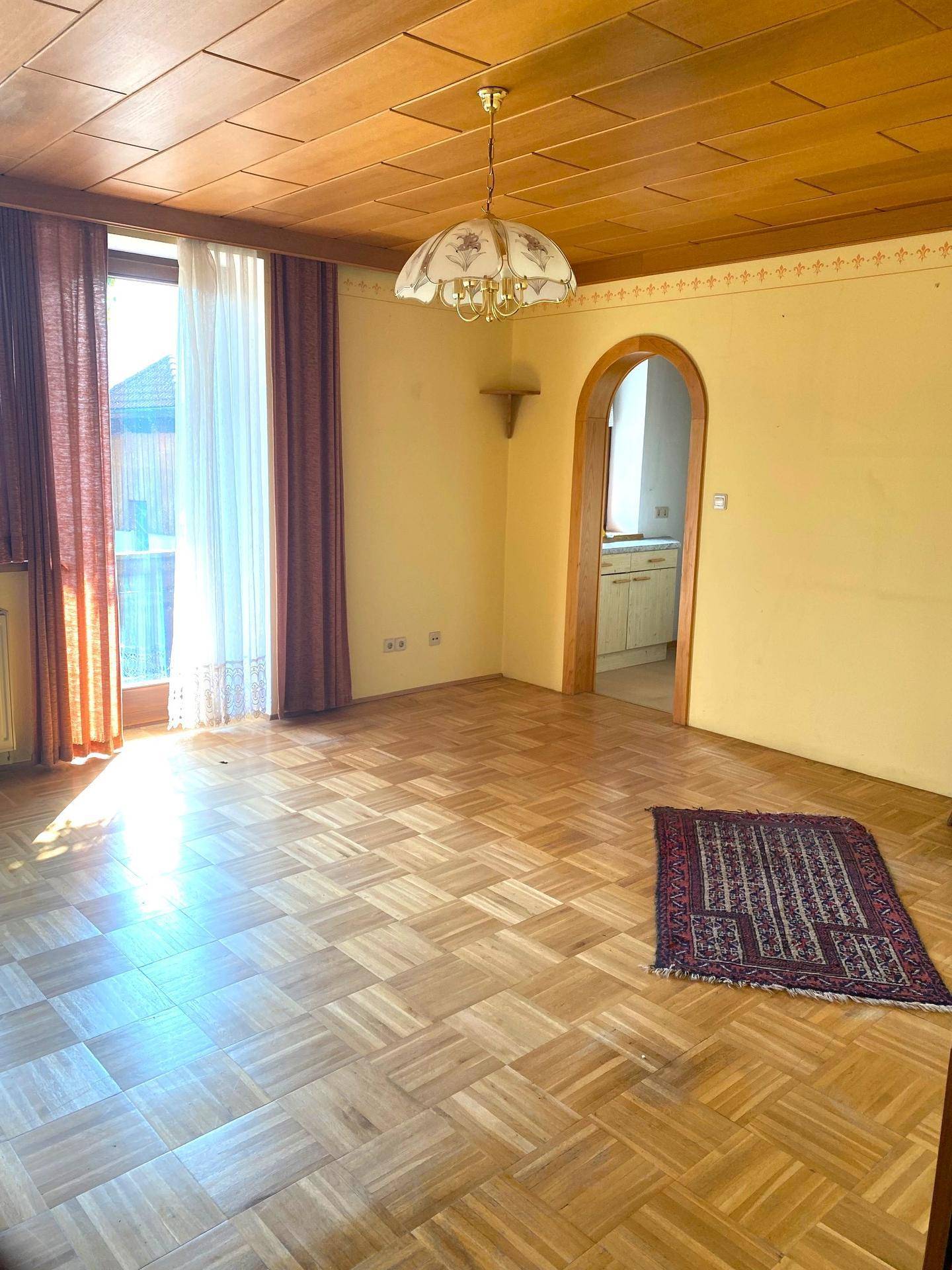 Helles Wohnzimmer mit Parkettboden, Holzdecke und einem charmanten Rundbogen zum nächsten Raum.