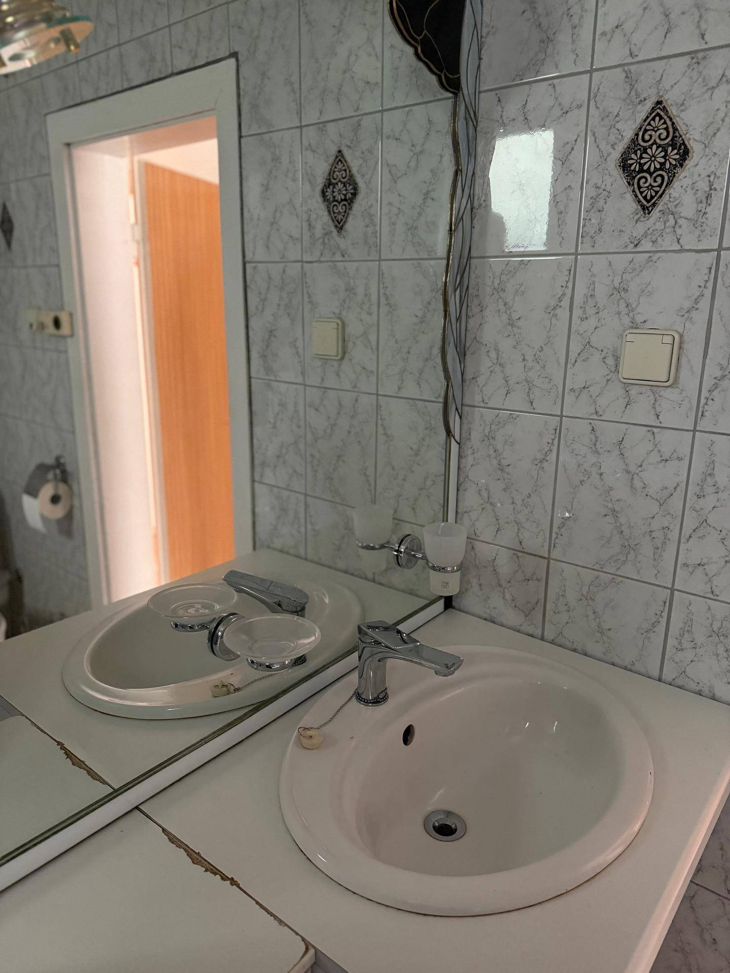 Badezimmer mit Waschbecken, großem Spiegel und gefliesten Wänden im Retro-Stil.