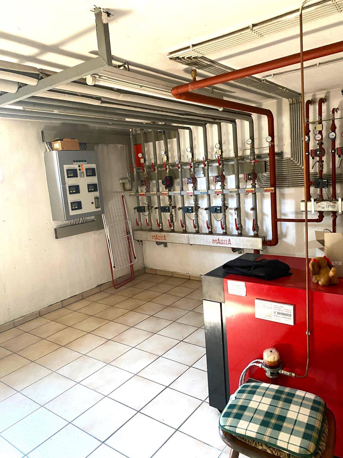 Technikraum mit Heizungsanlage, zahlreichen Rohren und Fliesenboden.
