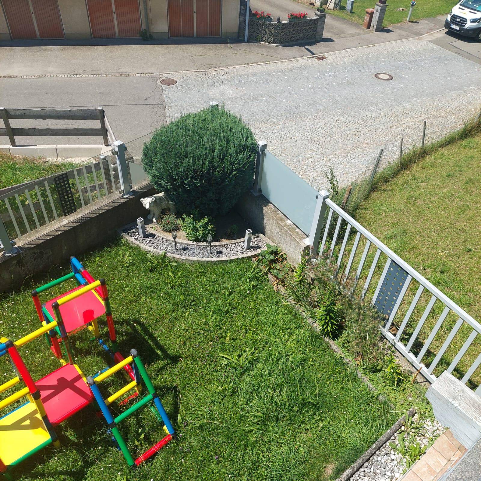 Garten mit Rasenfläche und bunten Spielgeräten für Kinder.