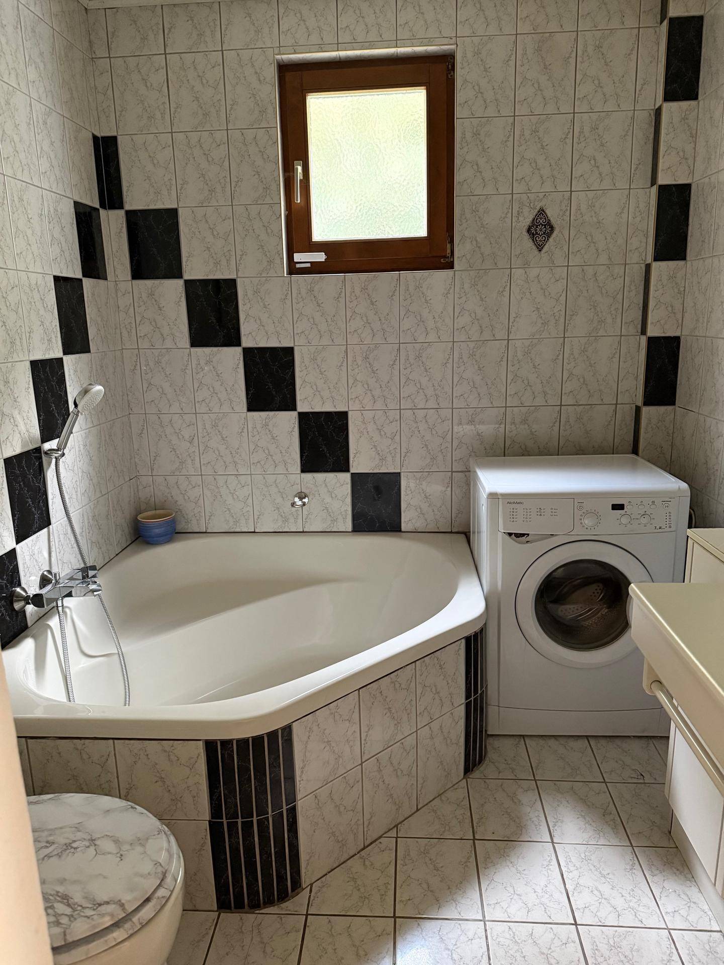 Badezimmer mit Eckbadewanne, Waschmaschine und schwarz-weiß gefliesten Wänden.