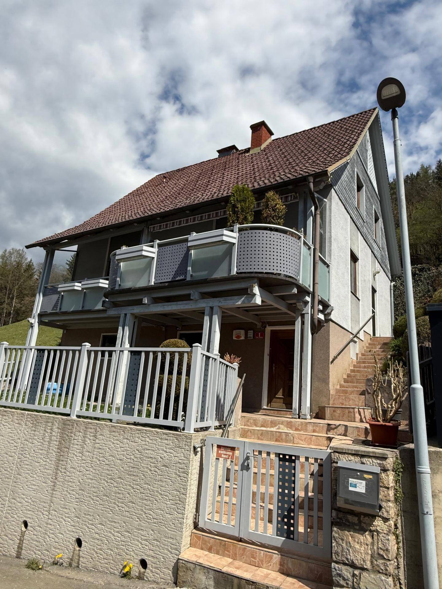 Vorderansicht des Hauses mit Eingangsbereich, Treppe und mehreren Balkonen.