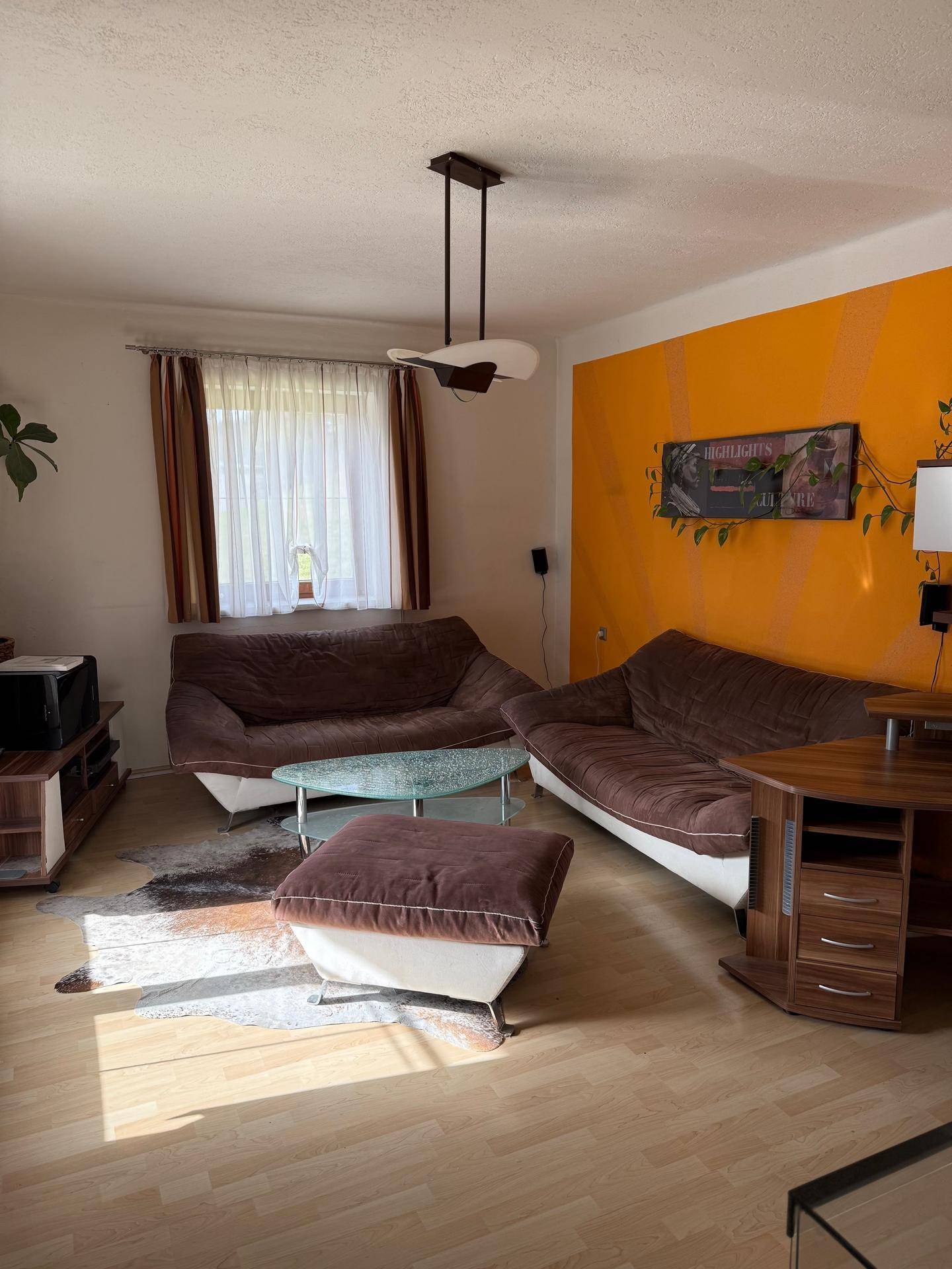 Gemütliches Wohnzimmer mit braunen Sofas, Holzboden und einer orangefarbenen Akzentwand.