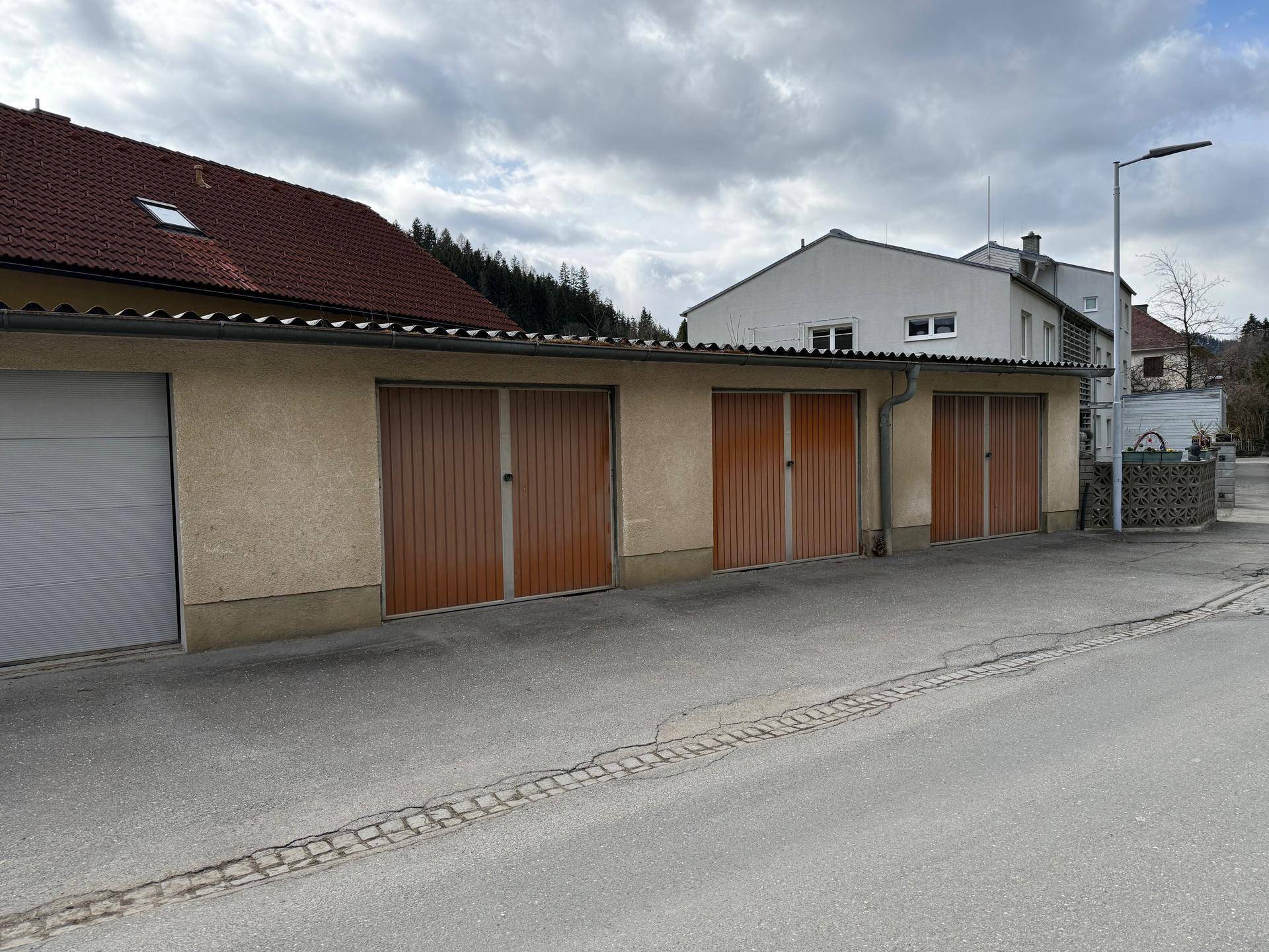 Reihe von Garagen mit Holztoren entlang einer ruhigen Wohnstraße.