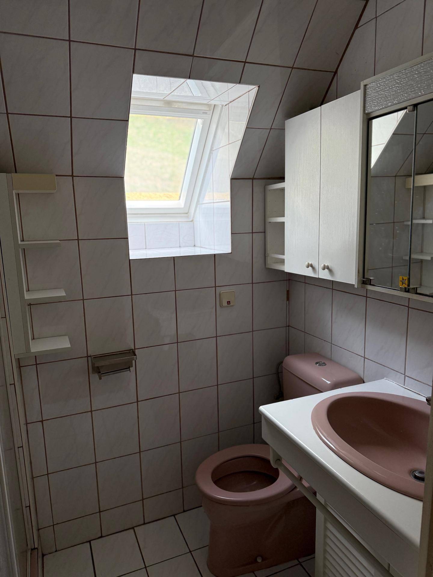 Dachschrägen-Badezimmer mit Dachfenster, rosa Sanitärobjekten und gefliesten Wänden.