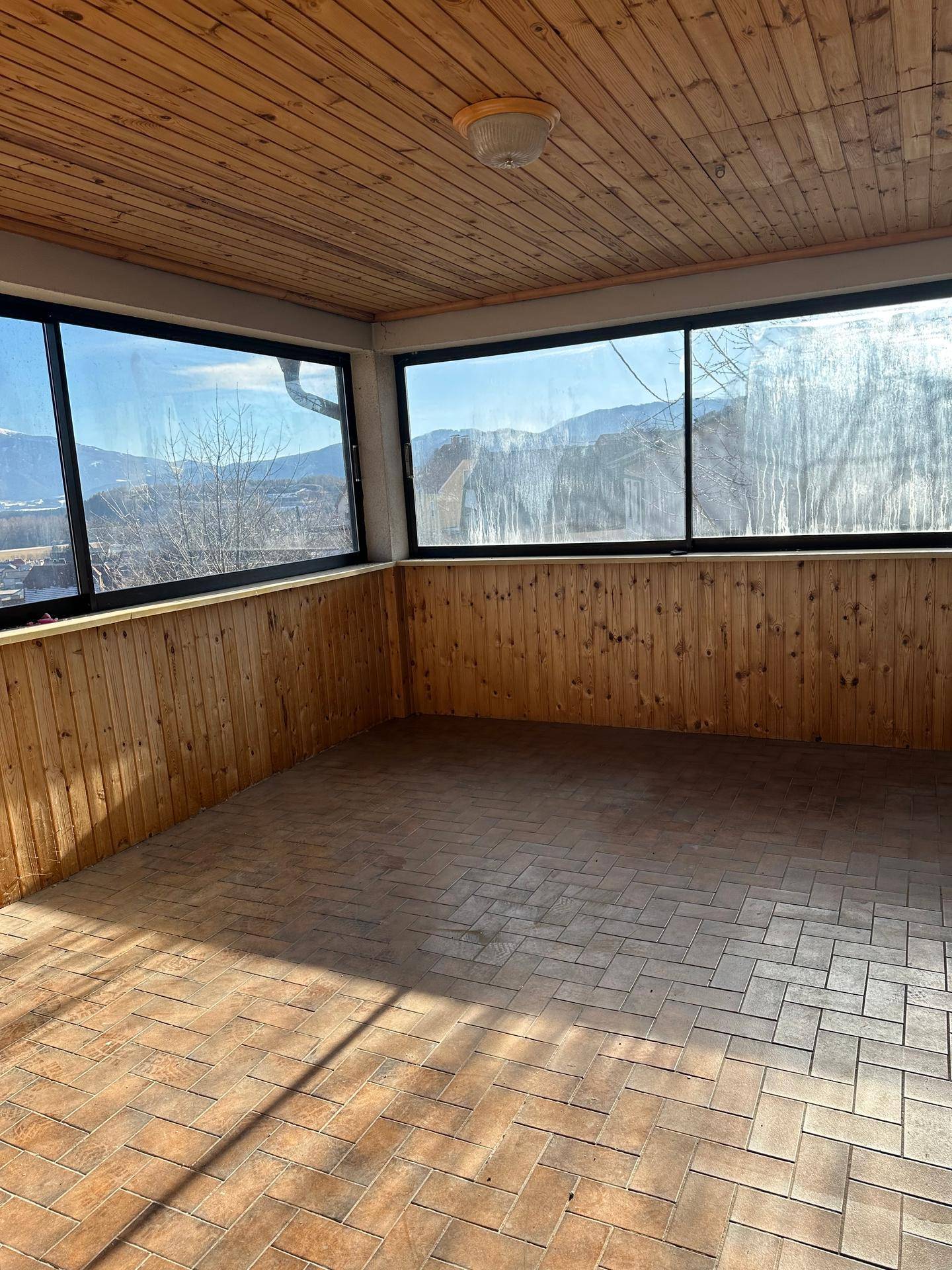 Heller Wintergarten mit Holzverkleidung an Wänden und Decke sowie großen Fenstern mit Bergblick.