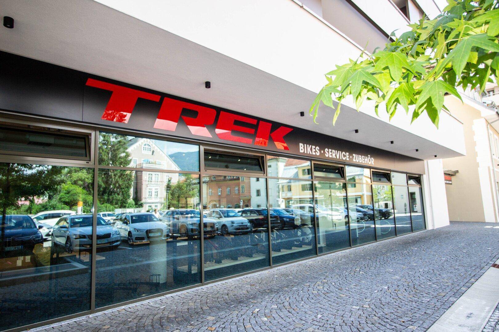 Eingangsbereich des Fahrradgeschäfts mit großer TREK-Beschriftung und reflektierenden Schaufenstern zur Straße.