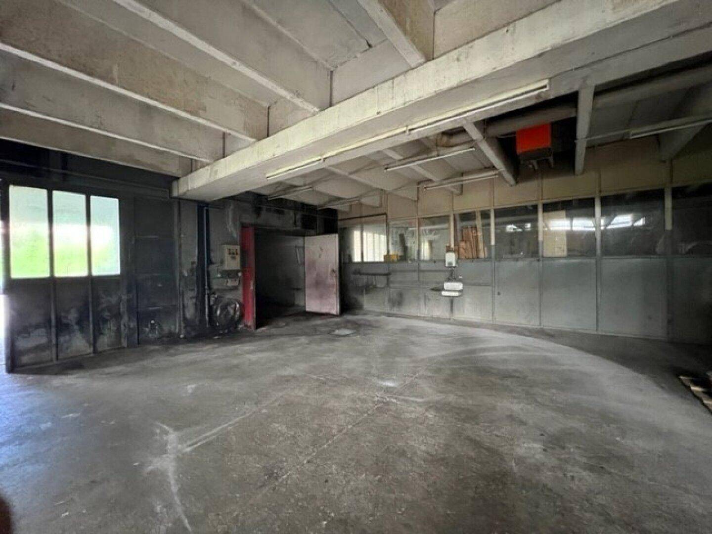 Geräumiger, leerer Lagerraum mit Betonboden, hohen Decken und Fenstern entlang einer Wand.