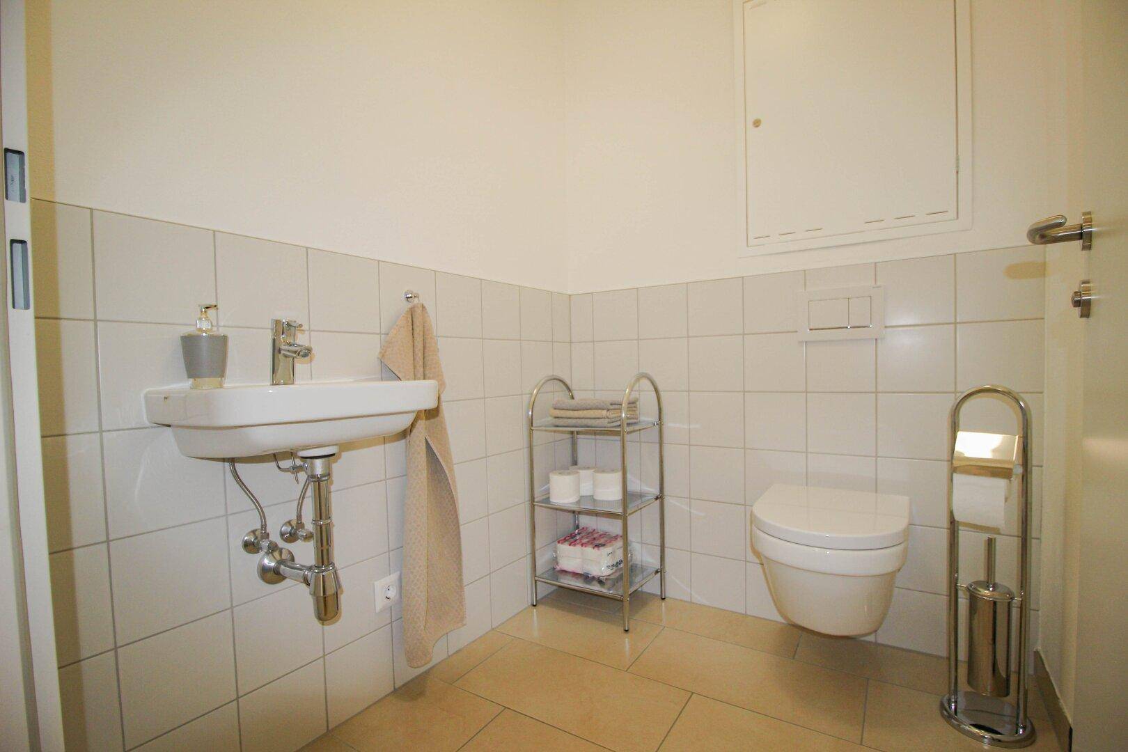 Modernes Gäste-WC mit weiß gefliesten Wänden, wandhängendem WC und einem kleinen Waschbecken.