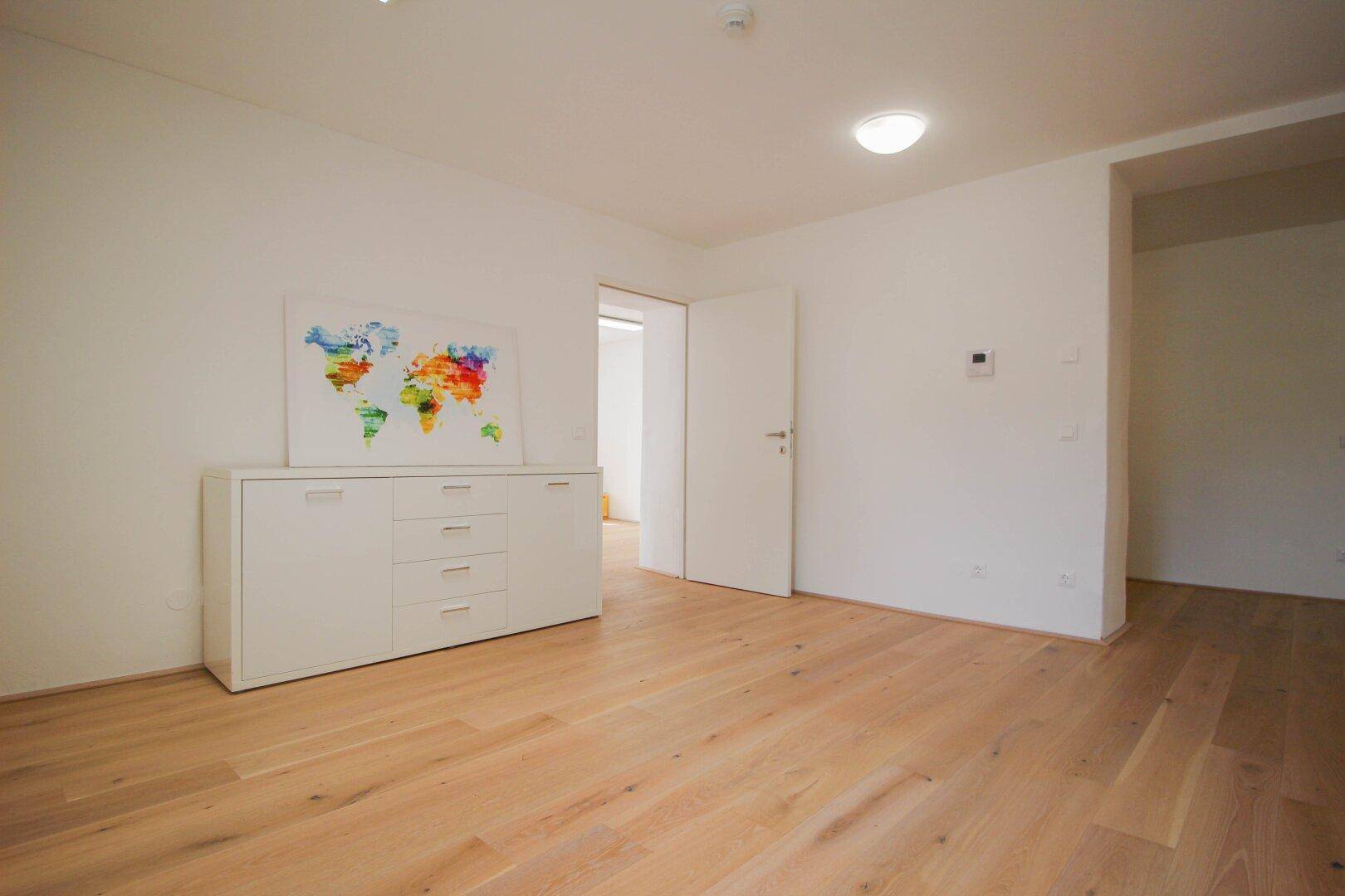 Heller Büroraum mit weißem Sideboard und Weltkartenbild, offener Tür und Holzboden.