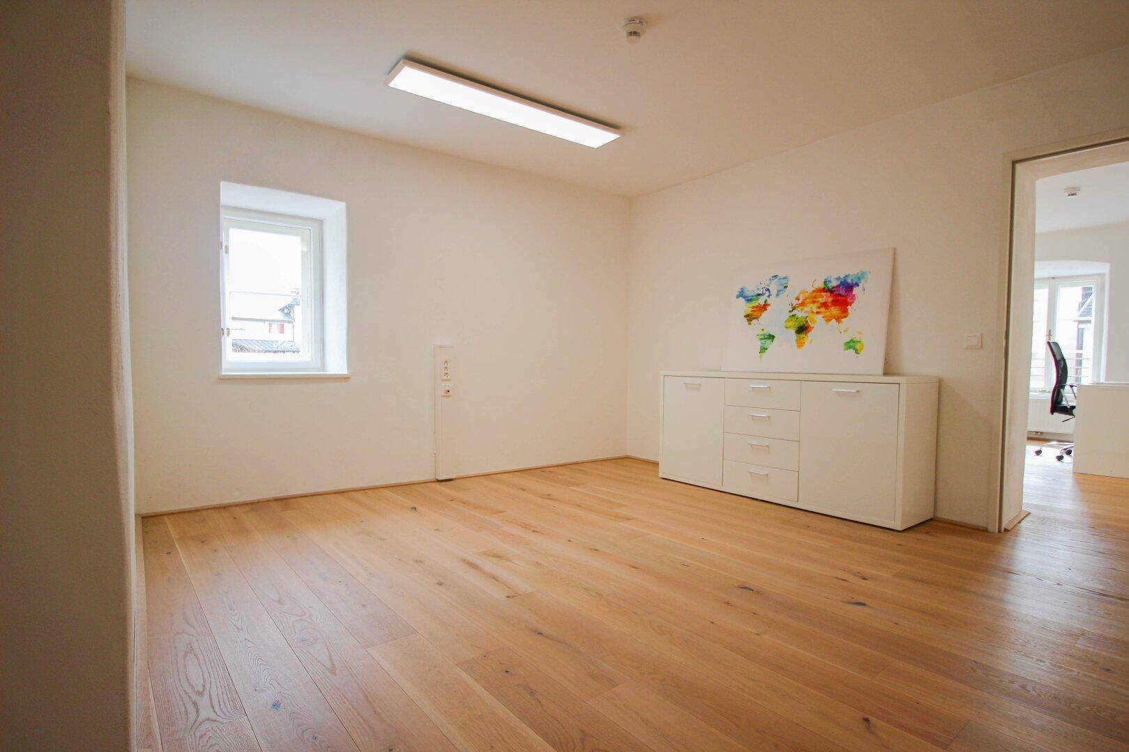 Heller Raum mit Holzboden, weißem Sideboard und einer Weltkarte, ideal als Empfangsbereich oder Büro.