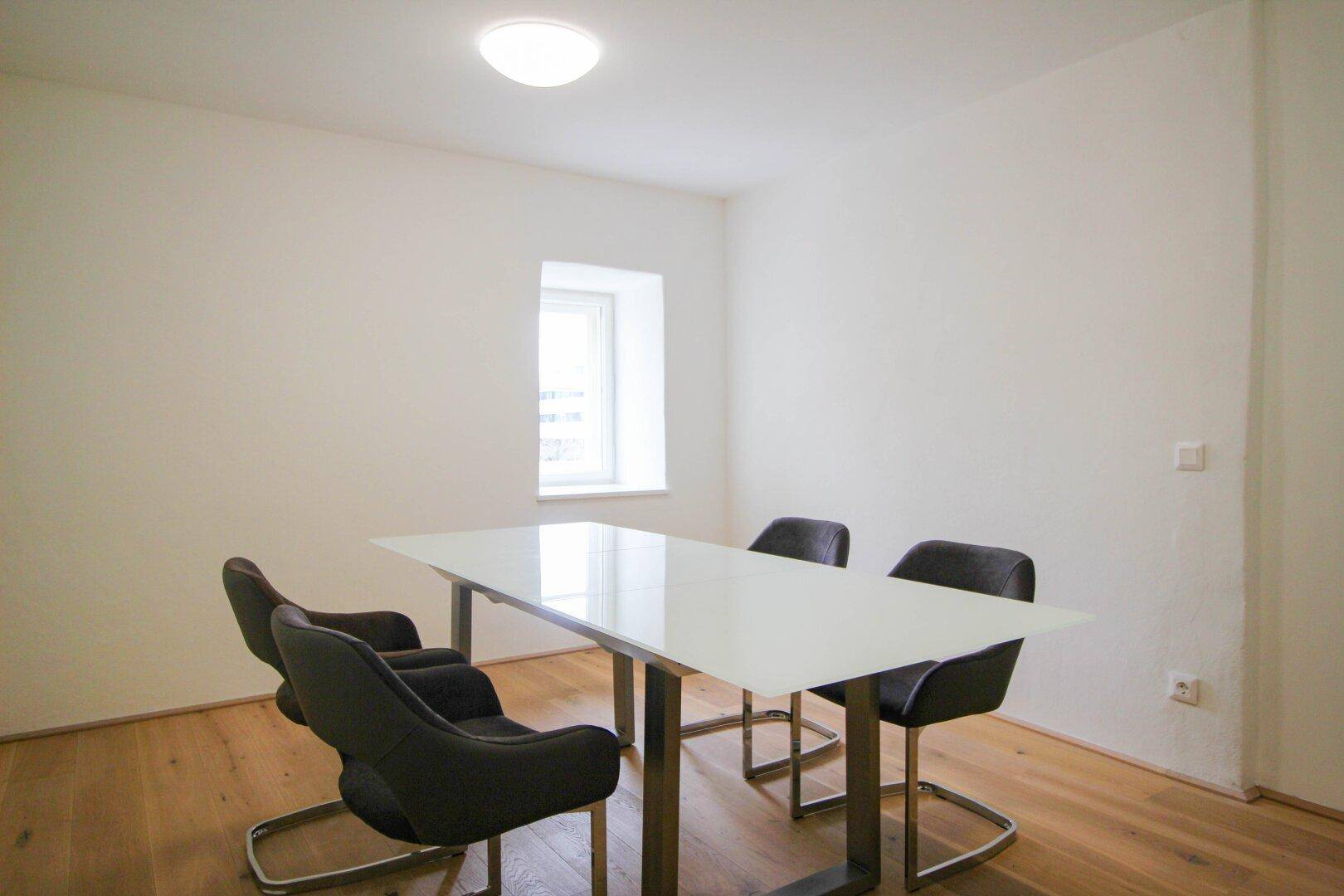 Modernes Ess- oder Besprechungszimmer mit weißem Tisch, vier Stühlen und hellem Holzboden.
