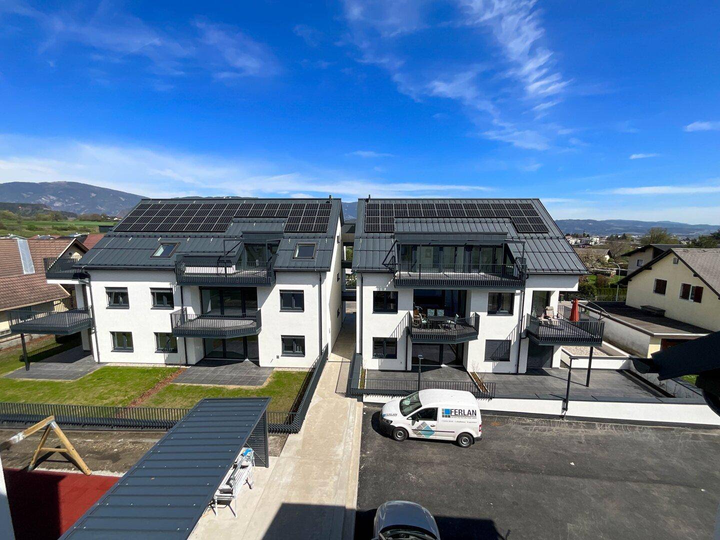 Zwei moderne Wohngebäude mit Solaranlagen auf den Dächern und Balkonen, umgeben von Grünflächen.